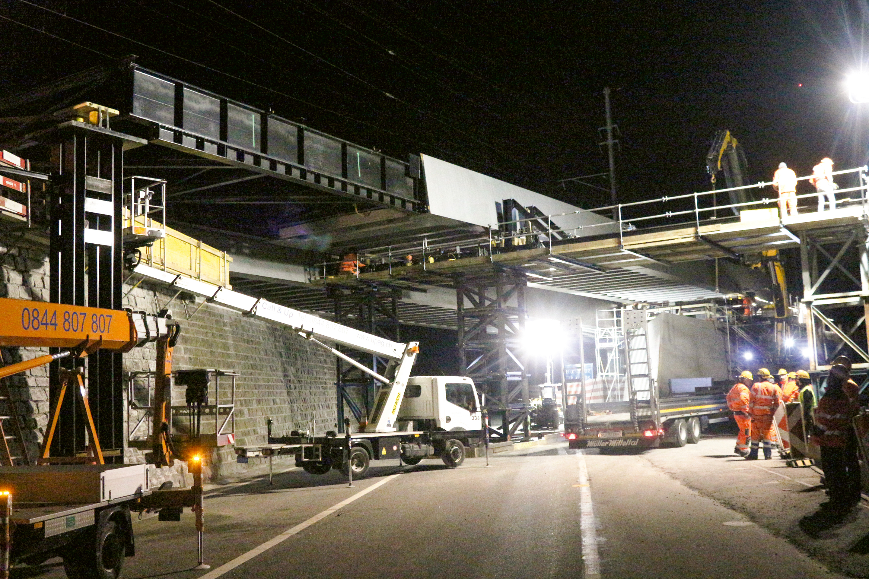 Zwischenstand um 1 Uhr morgens: Die Überführung steht hinten auf dem Widerlager und über der Nationalstrasse A13 auf zwei Hilfstürmen, wo die seitliche Führung der zweifach gekrümmten Brücke montiert wird. Rund 14 m auskragend und kurz vor dem nächsten Hilfsturm sind die mit einem Vorbauschnabel verlängerten Enden der Überführung zu sehen.