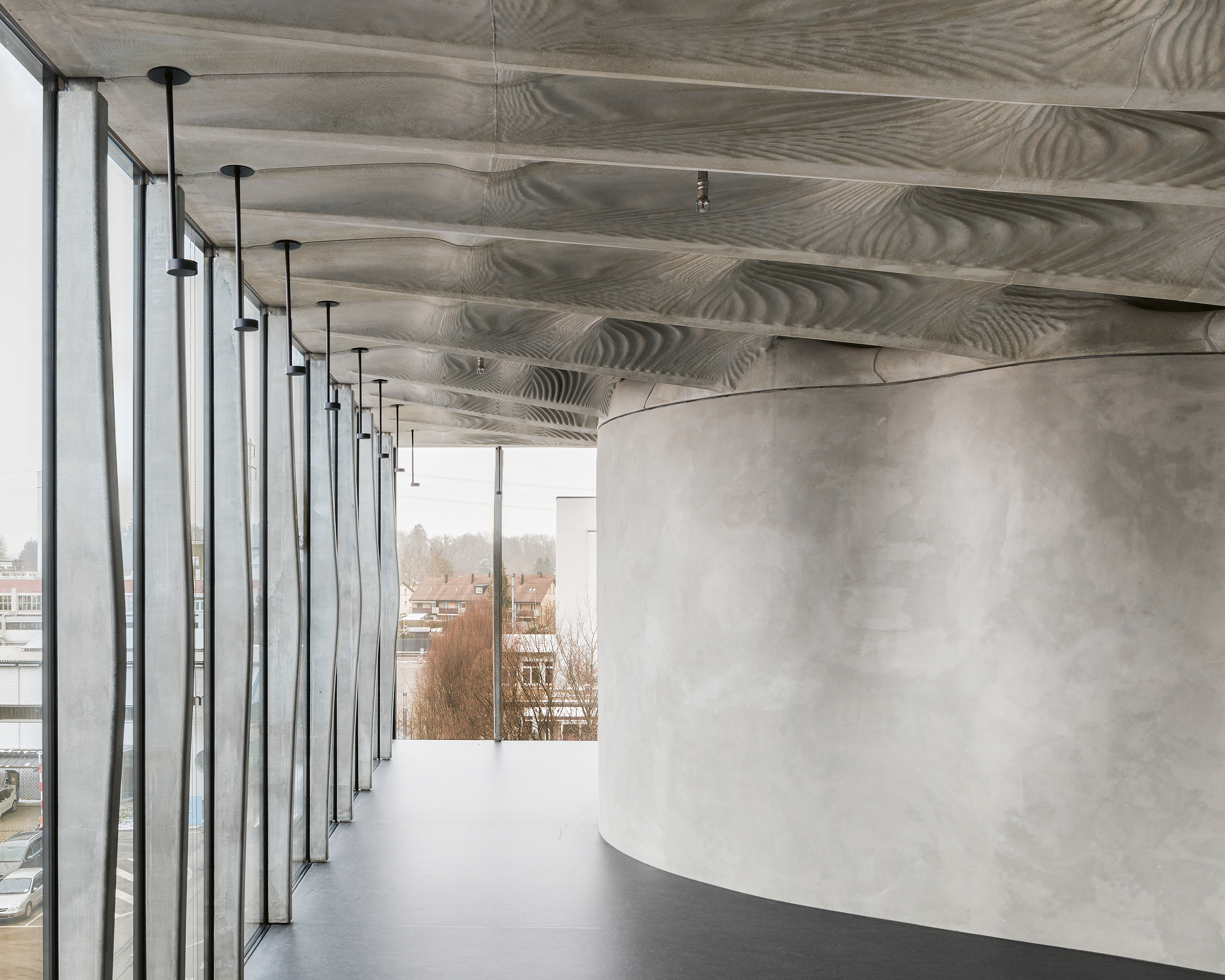 Die Betonstützen in der Fassade wurden vor Ort gefertigt. Zum Einsatz kam Smart Dynamic Casting, ein kontinuierliches, robotergesteuertes Gleitschalungsverfahren. Die doppelt gekrümmte Mesh-Mould-Wand trennt den Wohnbereich von der Küche und dem Eingang ab. Die Decke aus faserverstärktem Beton ist in Bezug auf die Statik und den Materialverbrauch optimiert, die Schalung wurde mit 3-D-Druck hergestellt.