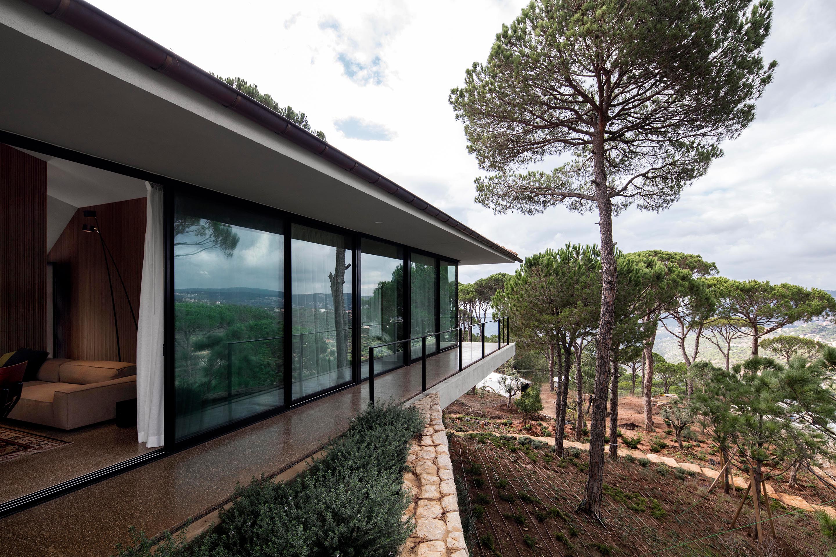 Die Nordfassade steht teilweise auf einer Steinstützmauer, die sich um das Haus herum erstreckt und den Terrassenbereich umfasst.