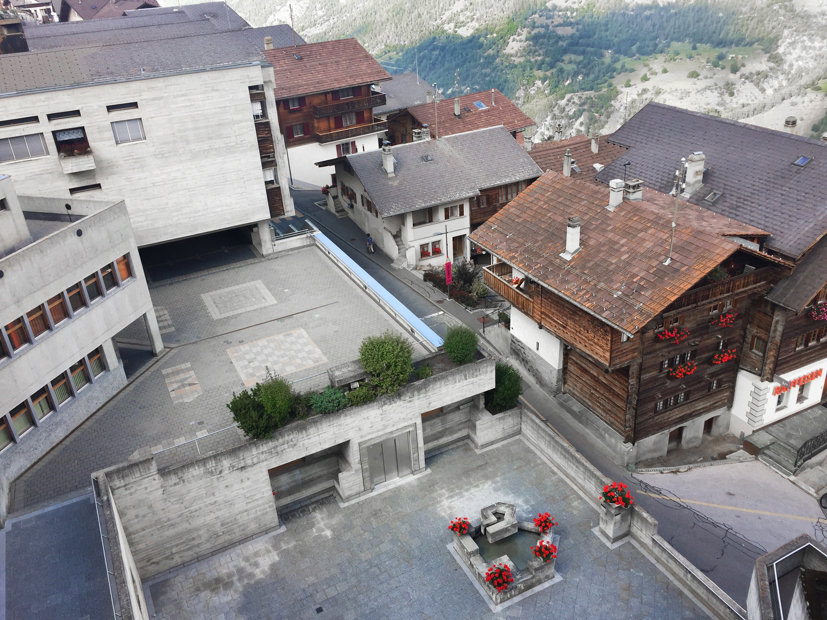 Blick vom Kirchturm: Der mit Geranien verzierte Brunnen steht vor dem Eingang der Kirche, weiter unten ist der Platz zum Gemeindehaus (nicht im Bild) zu erkennen.