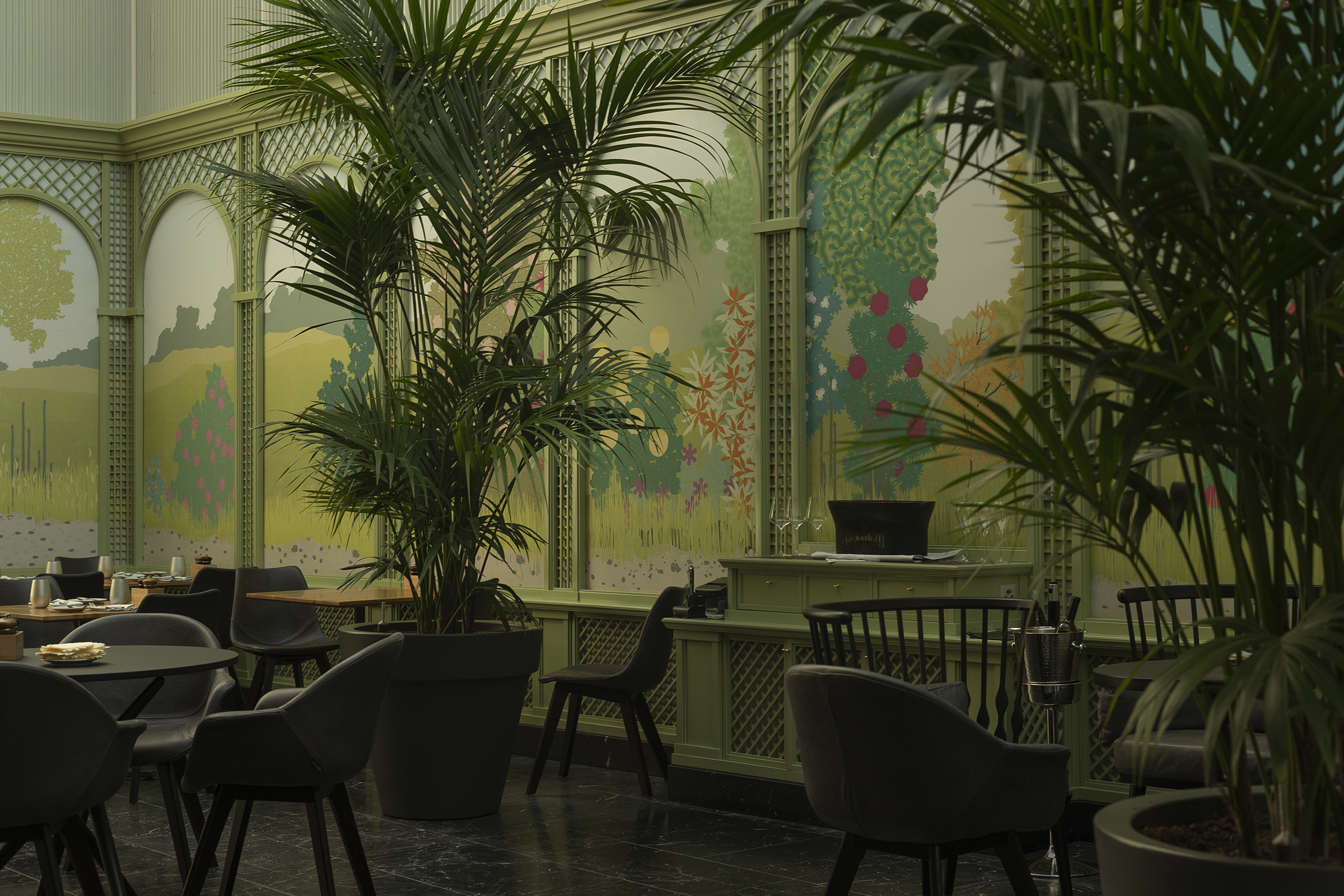 Der neu gestaltete Wintergarten: Zusammen mit dem bestehenden Steinboden bildet die frei arrangierbare Möblierung einen dunklen Fond, von dem sich die farbige Wandgestaltung abhebt. Üppige Pflanzen unterstützen die Illusion eines Gartenzimmers.