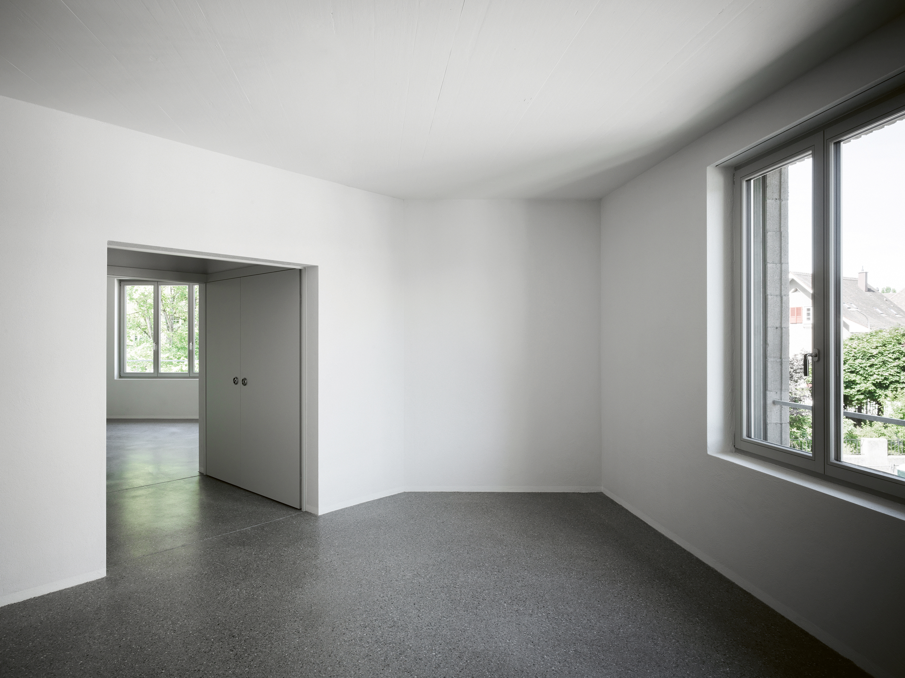 Der durchgängige Bodenbelag aus geschliffenem Hartbeton und die breite Öffnung betonen den Raumfluss. Seitlich ist das geschlossene Klappbad zu sehen.