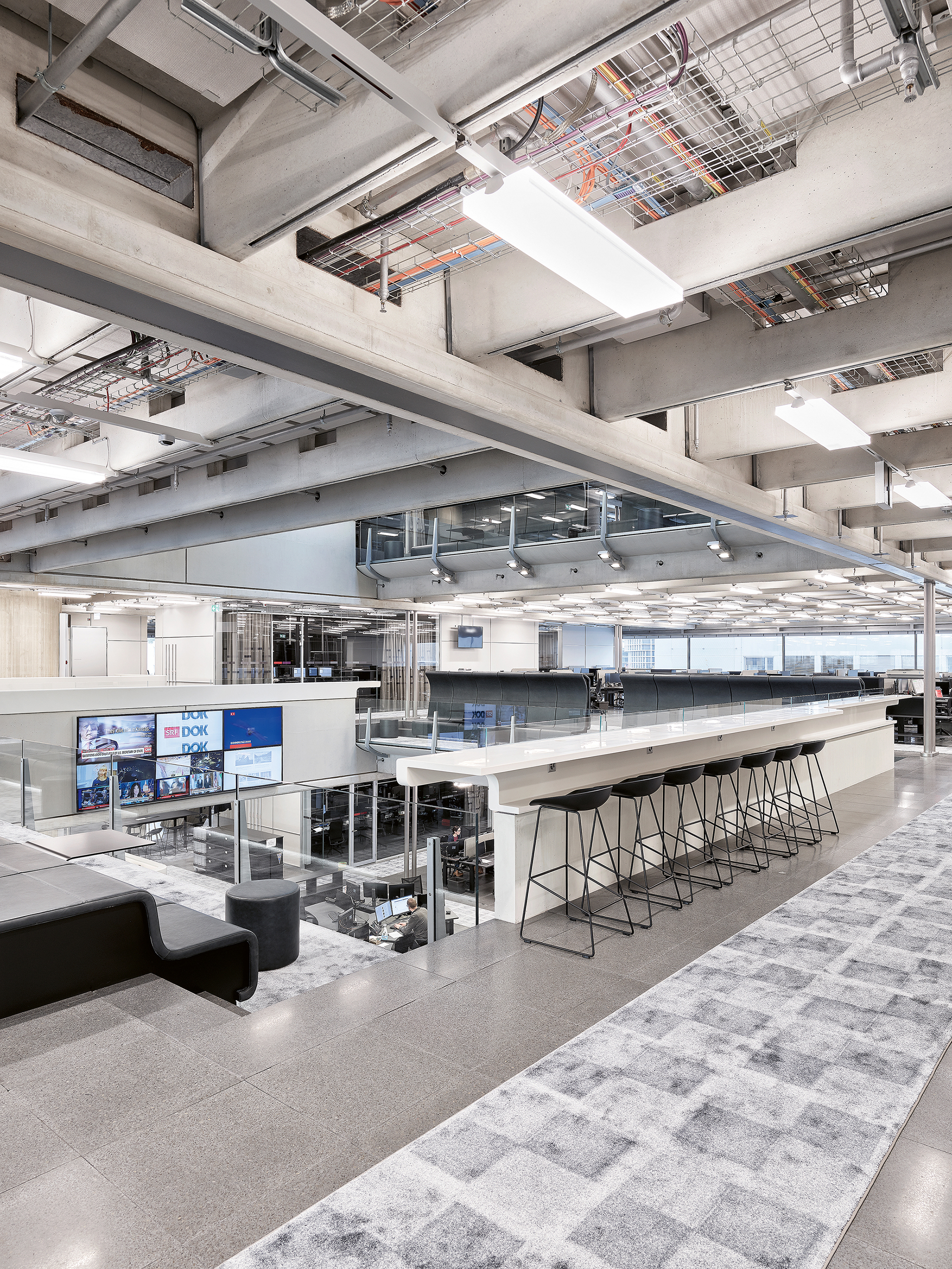 Medienarbeit als Qualitätshandwerk: Blick in das zentrale Atrium, um das sich die Arbeitsplätze im Newsroom gruppieren. Der Raum erhält Tageslicht durch die umlaufenden Bandfenster und das Oberlicht.