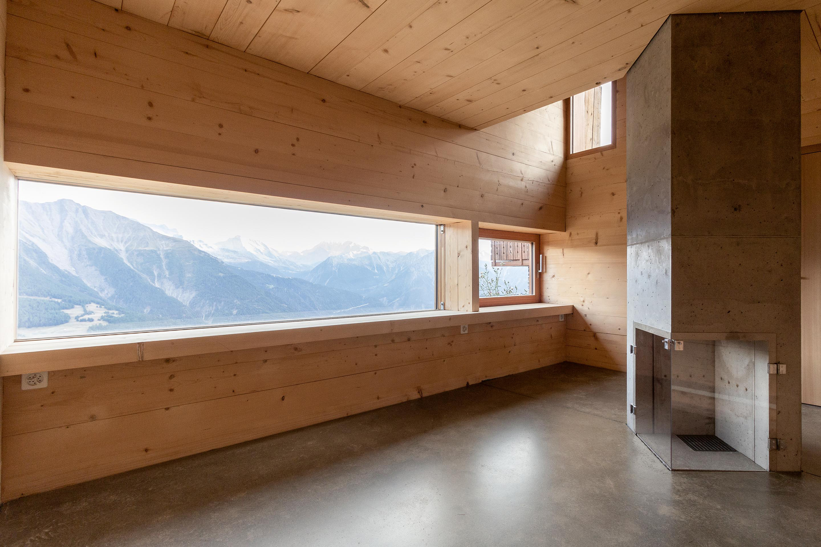Der moderne Innenraum des Ateliers auf der Riederalp zeichnet sich durch die massiven Strickholzwände, -treppen und -decken sowie  einen Ofen mit zweistöckigem Kamin aus.