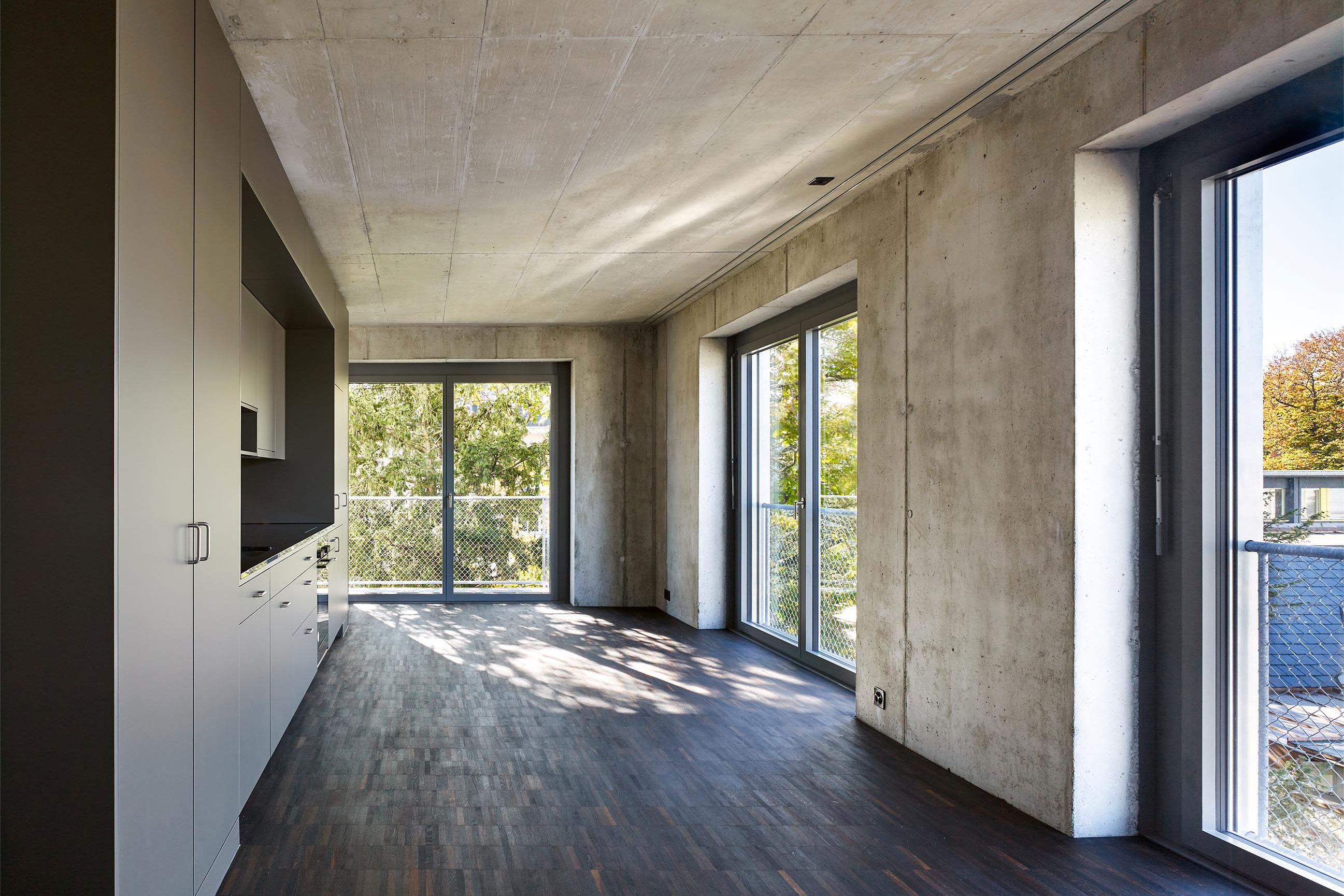 Dunkle Holzböden kontrastieren die rohen Betonwände und -decken. Das Einbaumöbel links gliedert den kompakten Wohnraum, schafft einen Rundgang und bietet Infrastruktur für Küche, Stauraum und einen Teil des Badezimmers.