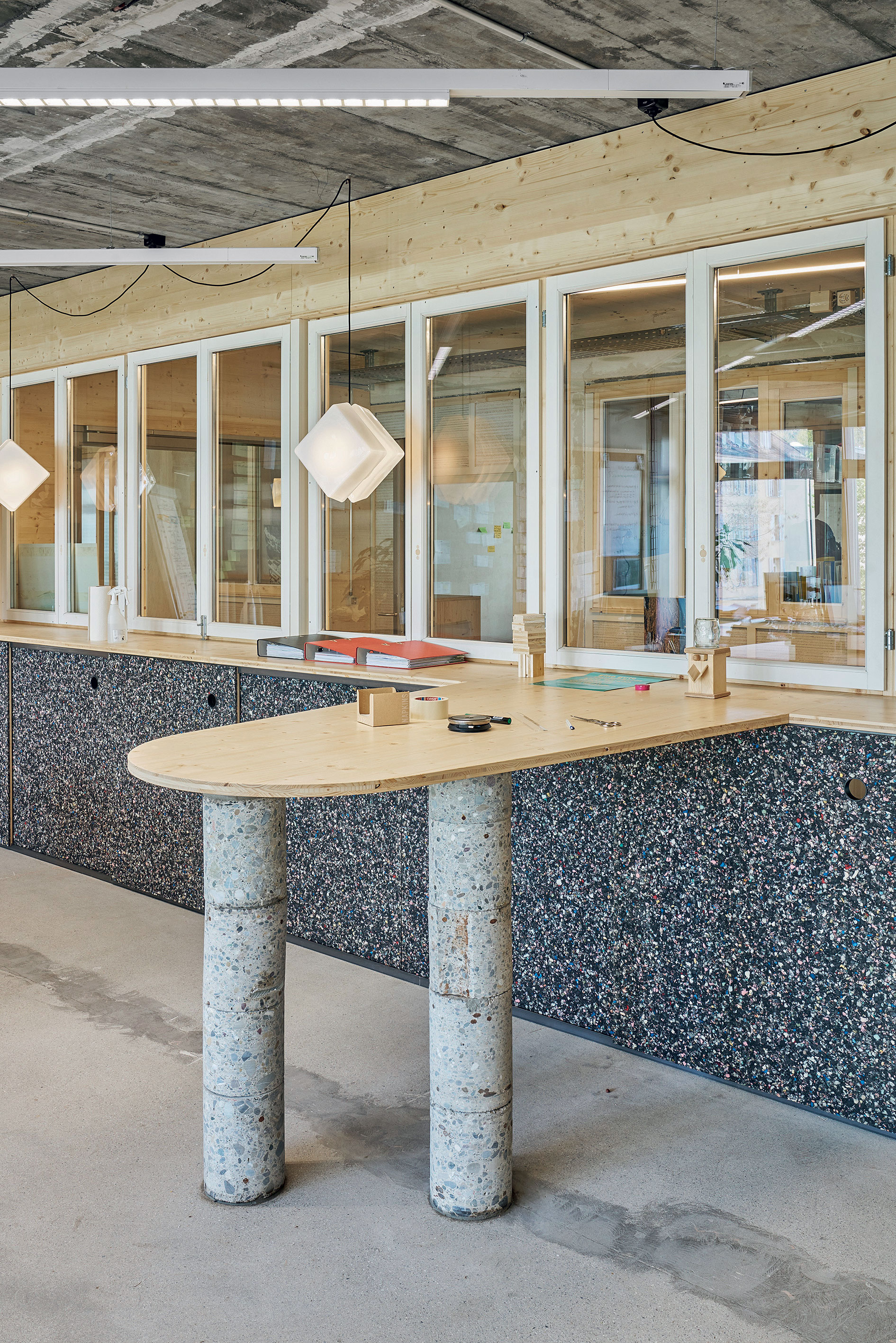 Des toilettes au bureau : les losanges blancs deviennent des lampes suspendues uniques en leur genre. Les fenêtres à coulisses des armoires sont des déchets plastiques réemployés.