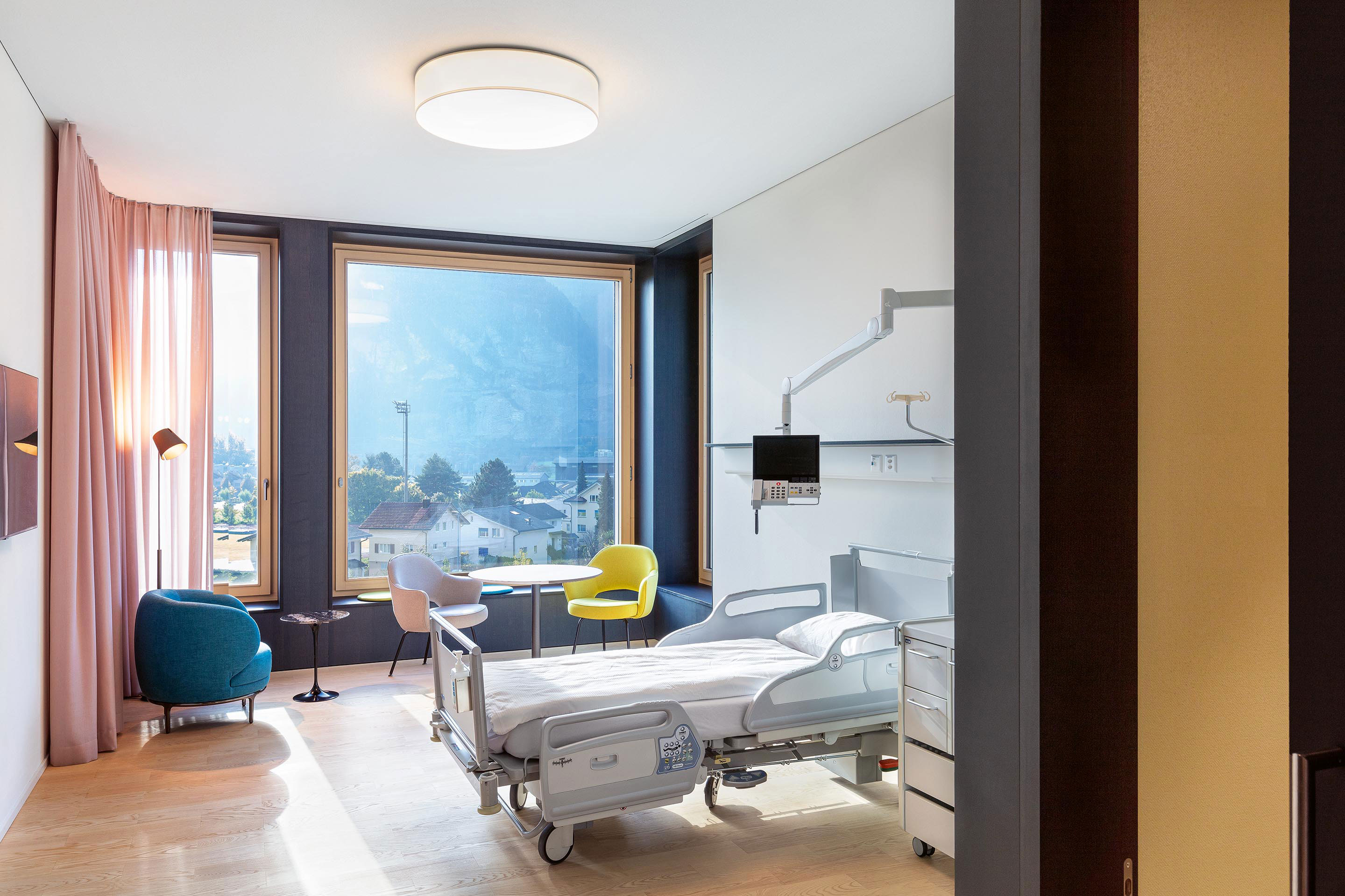 Vom Korridor der Bettenstation mit farbigen Wänden und eingefärbten Betonelementen öffnet sich der Blick in die wohnlichen Patientenzimmer und weiter in die Innerschweizer Berglandschaft.