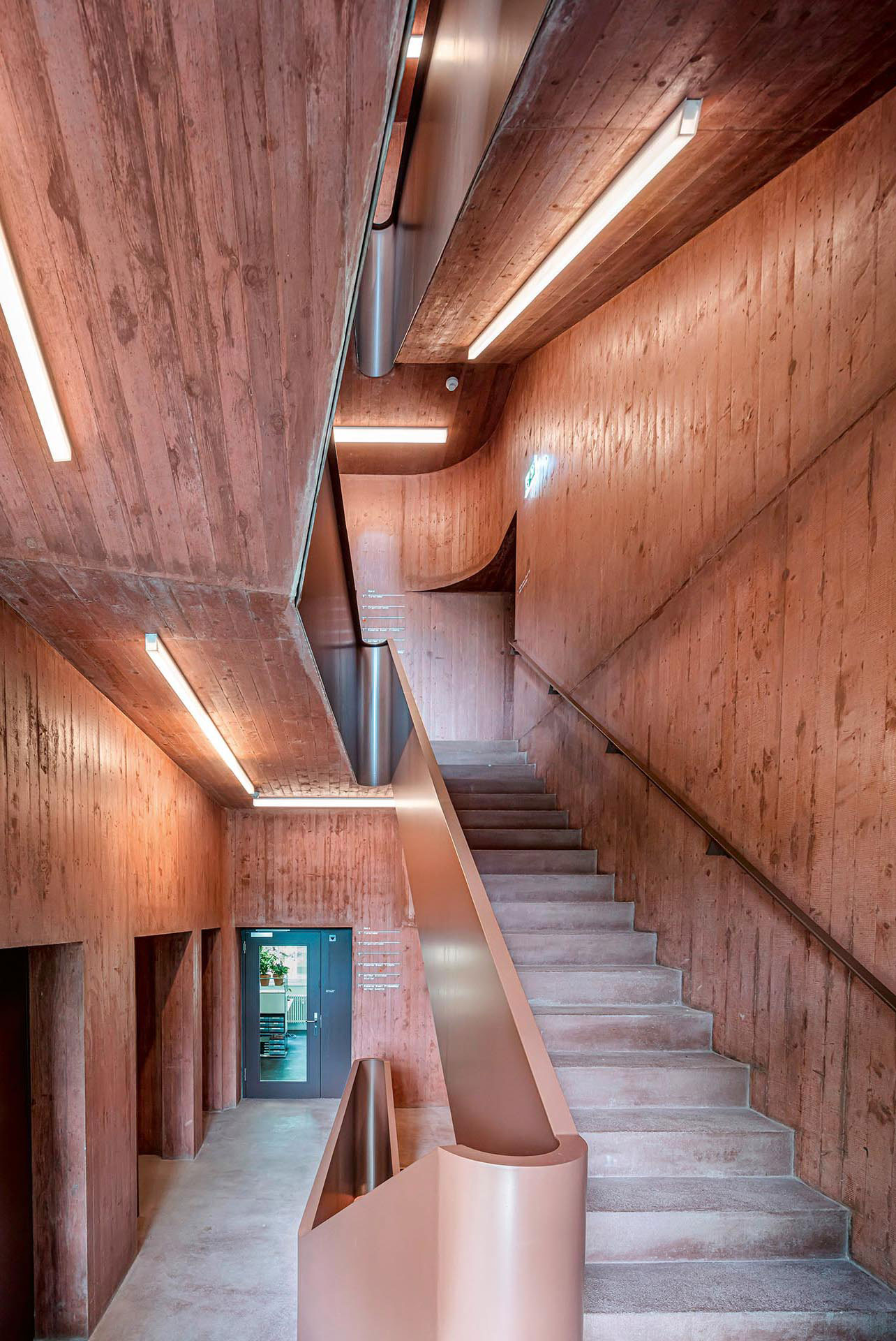 Erdige Rottöne ziehen sich auch ins Innere des Bauwerks: die neue, wie gefaltet wirkende Treppe aus Sichtbeton im Seitenflügel.