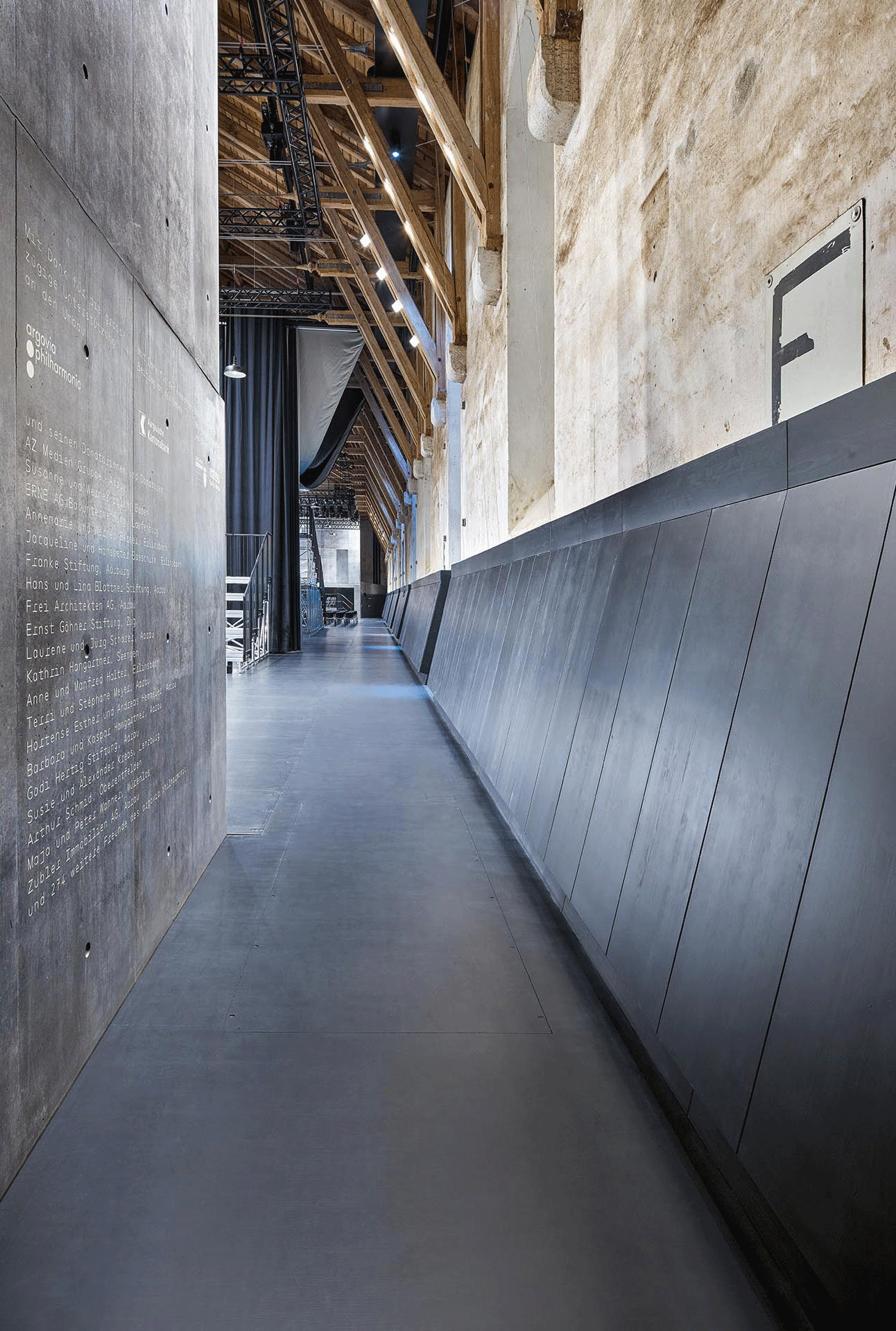 Die Holzverblendung der Aussenwände ist perforiert und hinterdämmt, um akustisch wirksam zu sein. Die ehemalige Reitspur geleitet zum mobilen Empfang, zur Backstage  oder zu den Sitzplätzen.