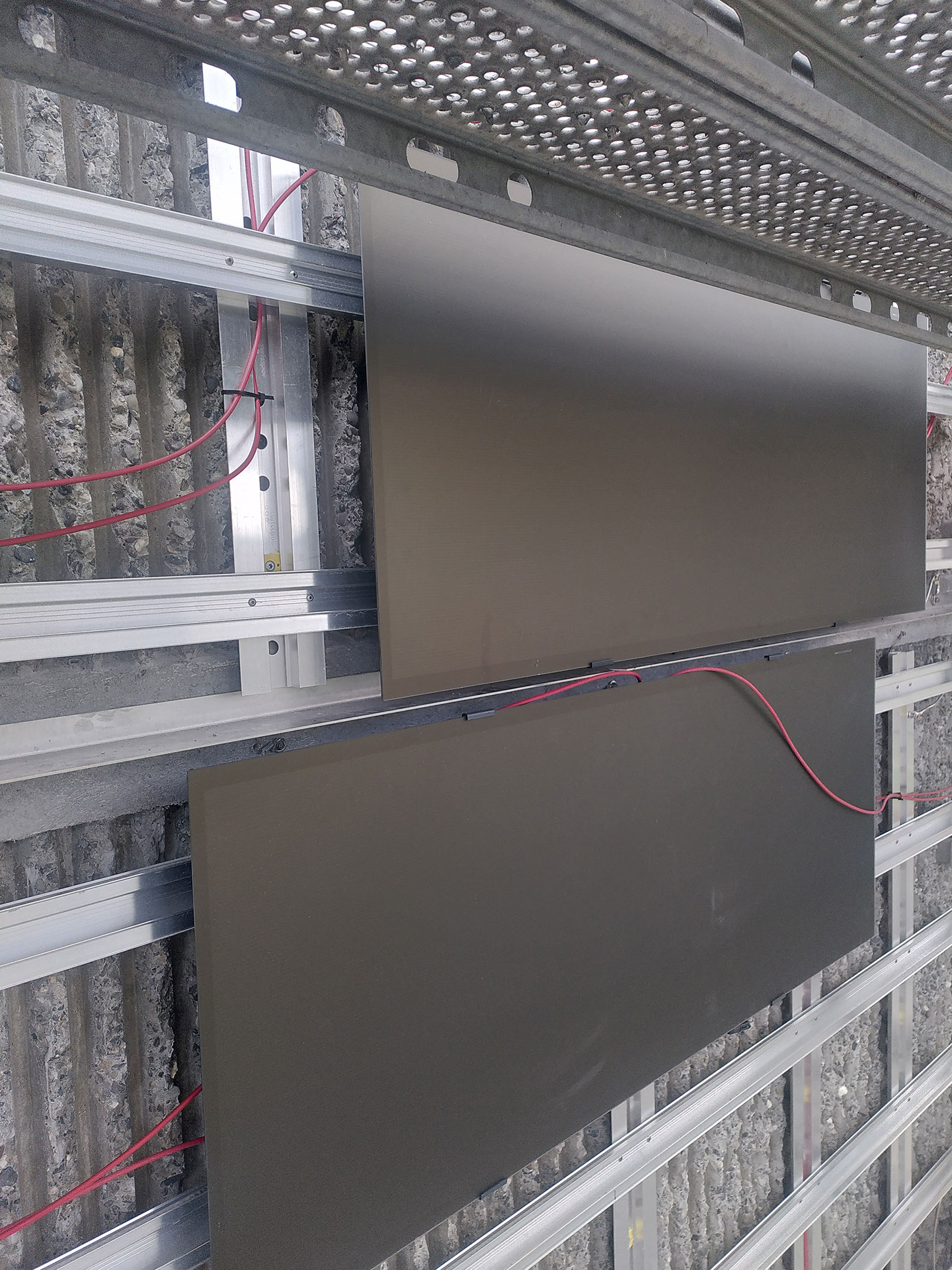 Blick hinter die auf Brandschutz optimierte Photovoltaikfassade kurz vor dem Einbau: Horizontale Chromstahlblenden sollen den Brandüberschlag verhindern, und Elektrokabel werden seitlich weggeführt.