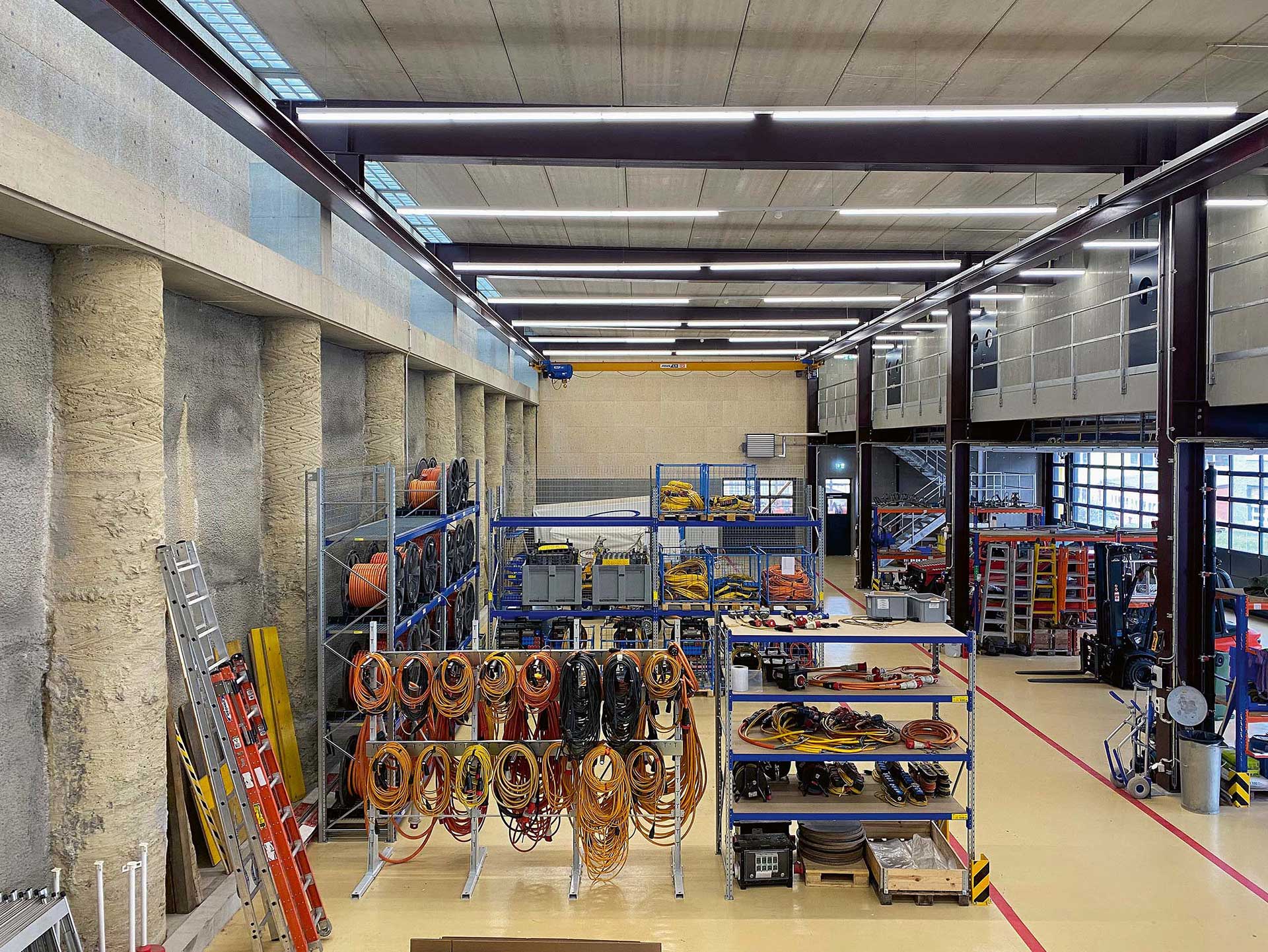 Stahltragwerk mit Oberflächenschutz: Das Stahltragwerk rhythmisiert den Innenraum, ist links auf der Bohrpfahlwand aufgelagert und rechts mit der Mittelstütze biegesteif verbunden. Die Hauptträger ziehen sich weiter durch den Büroraum zur Fassade auf der Gebäudevorderseite, wo die Träger jeweils an die Fassadenstütze angehängt sind.