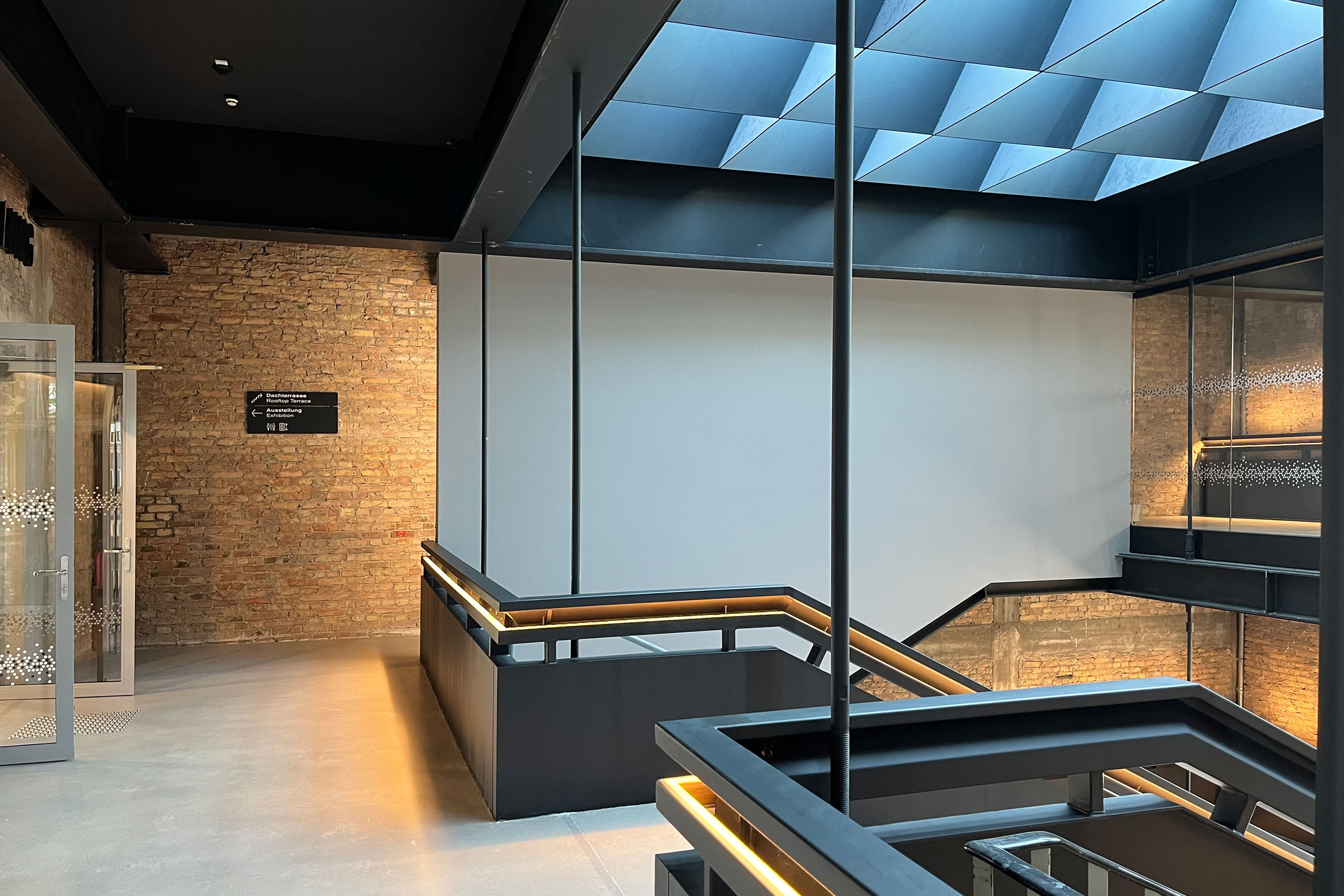 Tageslicht fällt durch die Stahlkonstruktion in den Treppenturm. Links hinter den Glastüren beginnt der Ausstellungsbereich.