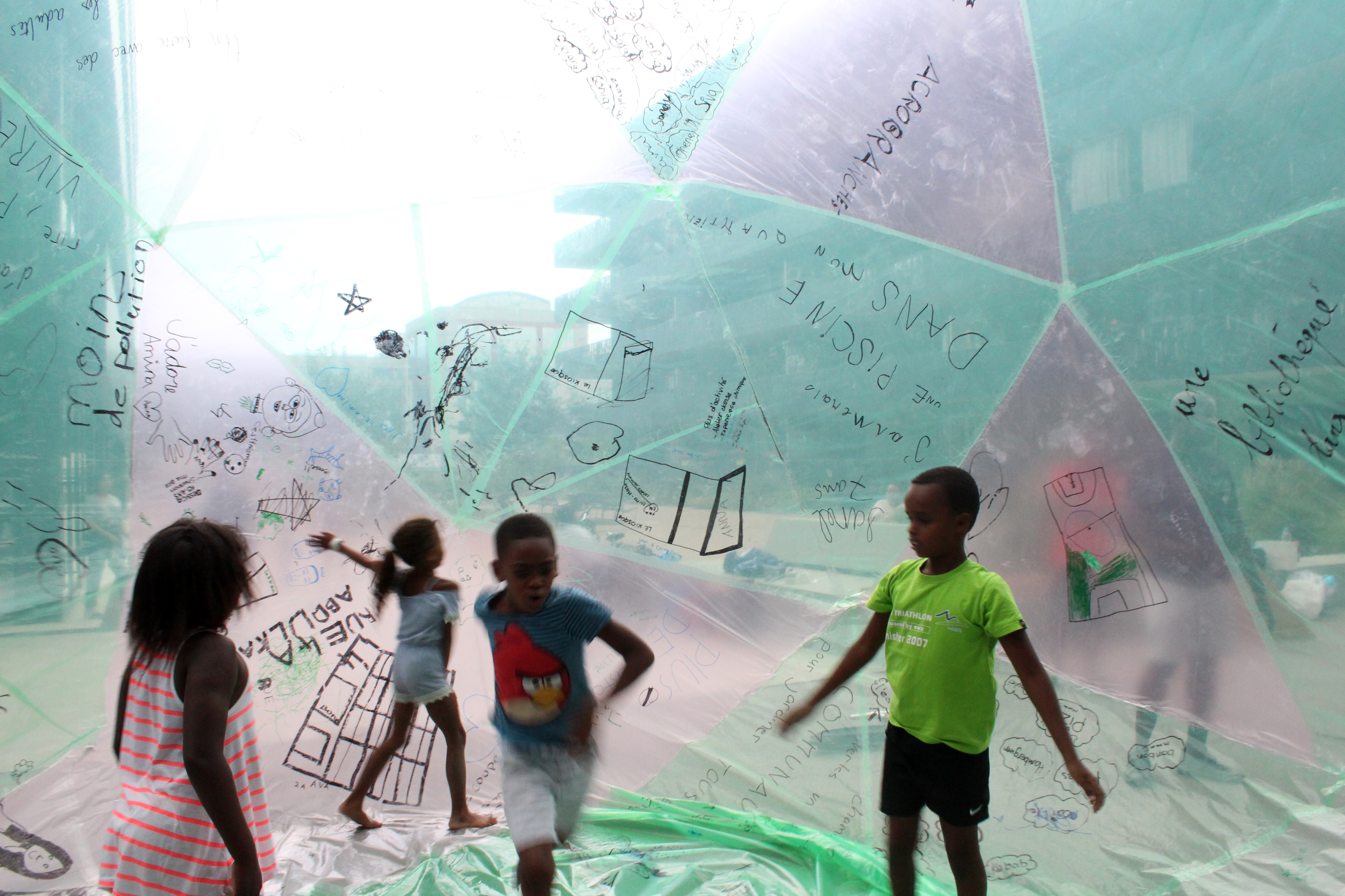 Grande Bulle à Gordon Bennett : un dispositif pour inviter les habitant·es à participer à la conception de la bulle (dessins, écriture, découpages, collage). Ils/elles ont été sollicités pour écrire sur chaque segment de plastique constituant la bulle, un mot invoquant leur rêve pour leur quartier. Dès que la bulle a été gonflée, enfants et adultes ont pu entrer et se déplacer à l’intérieur. Chacun​ ​a​ ​​​pu​ ​regarder​ ​les​ ​dessins,​ ​les​ ​rêves,​ ​les​ ​désirs​ ​sous​ ​un​ ​autre​ ​angle.