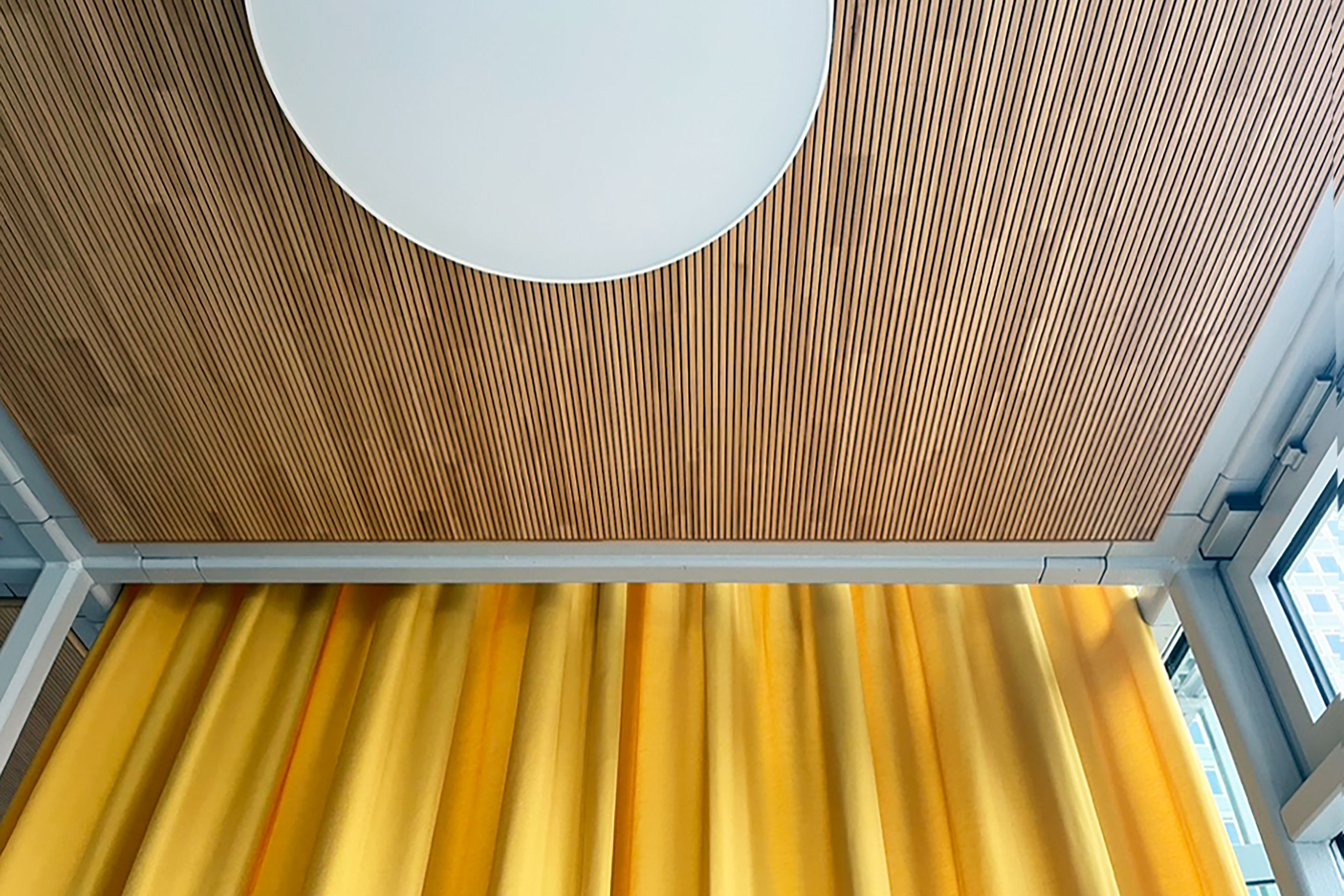 Les panneaux de bois au plafond viennent rompre l’atmosphère froide et contrastent avec le jaune des rideaux