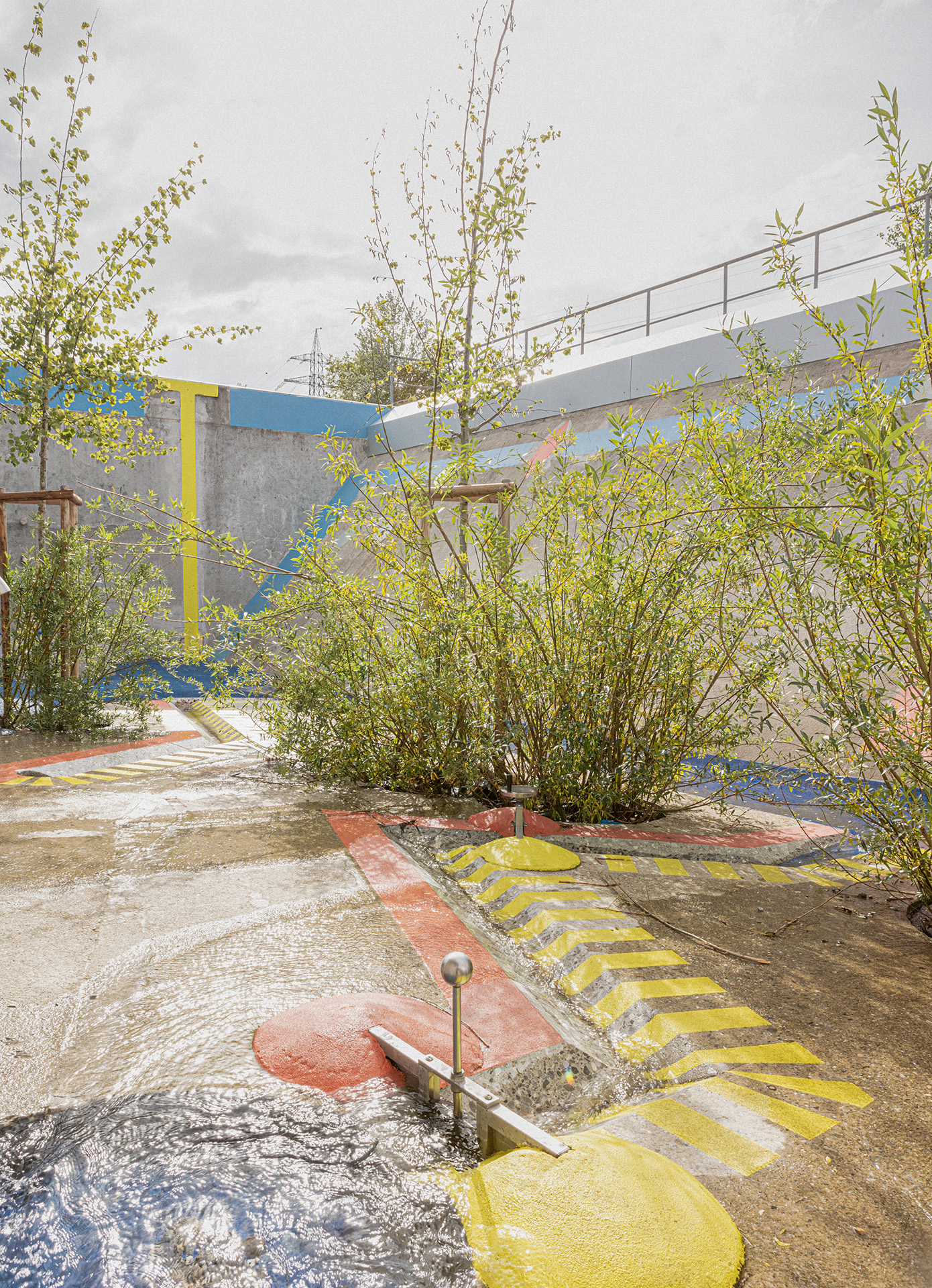 La végétation et les jeux d’eau apportent de la fraîcheur dans cet univers minéral. À terme, le pin de l’entrée et les peupliers trembles dépasseront de la construction pour faire appel et procurer de l’ombre. Au sol, les touffes de saules participent aux jeux.