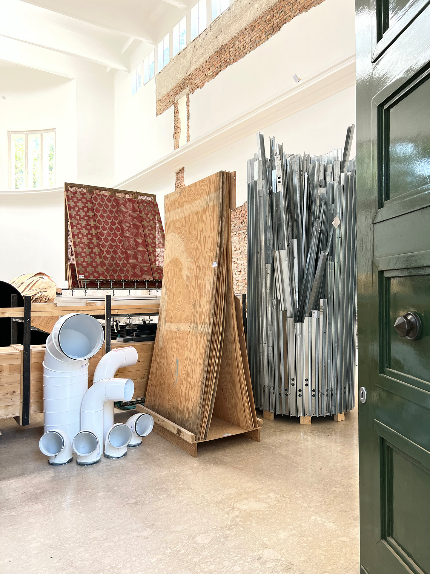 Blick von der schweren Eingangstür des Pavillons in den Hauptraum des Deutschenpavillons. Zwei Ausstellungsbeiträge überlagern sich im Gebäude. Im Hintergrund die von Maria Eichhorn freigelegten Schnittstellen des alten (1909) und neuen Deutschen Pavillons (1938). Im Vordergrund die recycelten Materialien des Beitrags von  ARCH+, Summacumfemmer/ Büro Juliane Greb aus dem Jahr 2023.