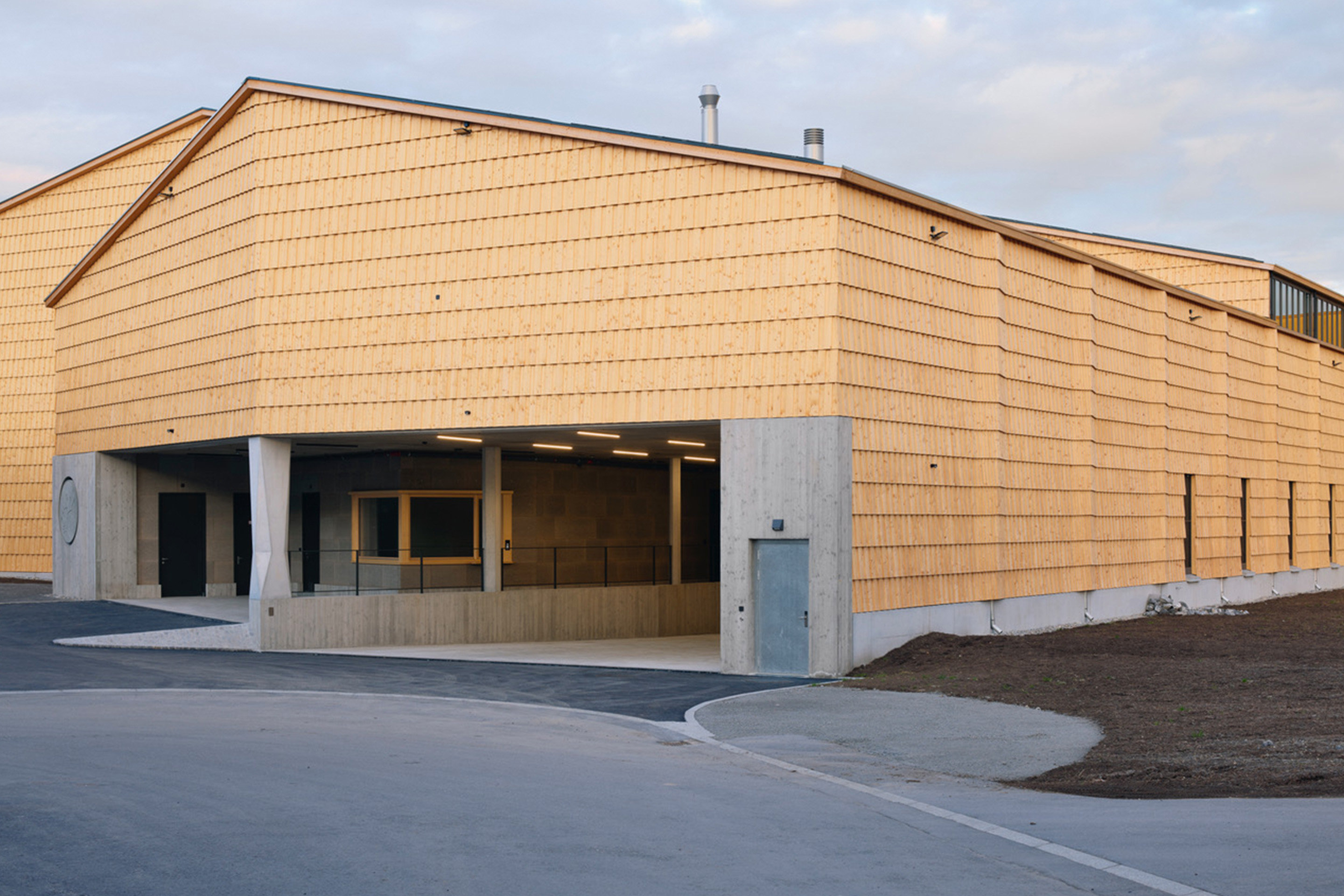 Als Ankündigung der innen liegenden Stützenachse steht bereits im Aussenraum eine Betonstütze. Zwischen der Portiersloge und dem Tor zur Anlieferung bietet ihre facettierte Gestalt von allen Seiten eine andere Ansicht und schlägt als Zitat einer gedrechselten Holzsäule den Bogen zur regionalen Handwerkskunst.