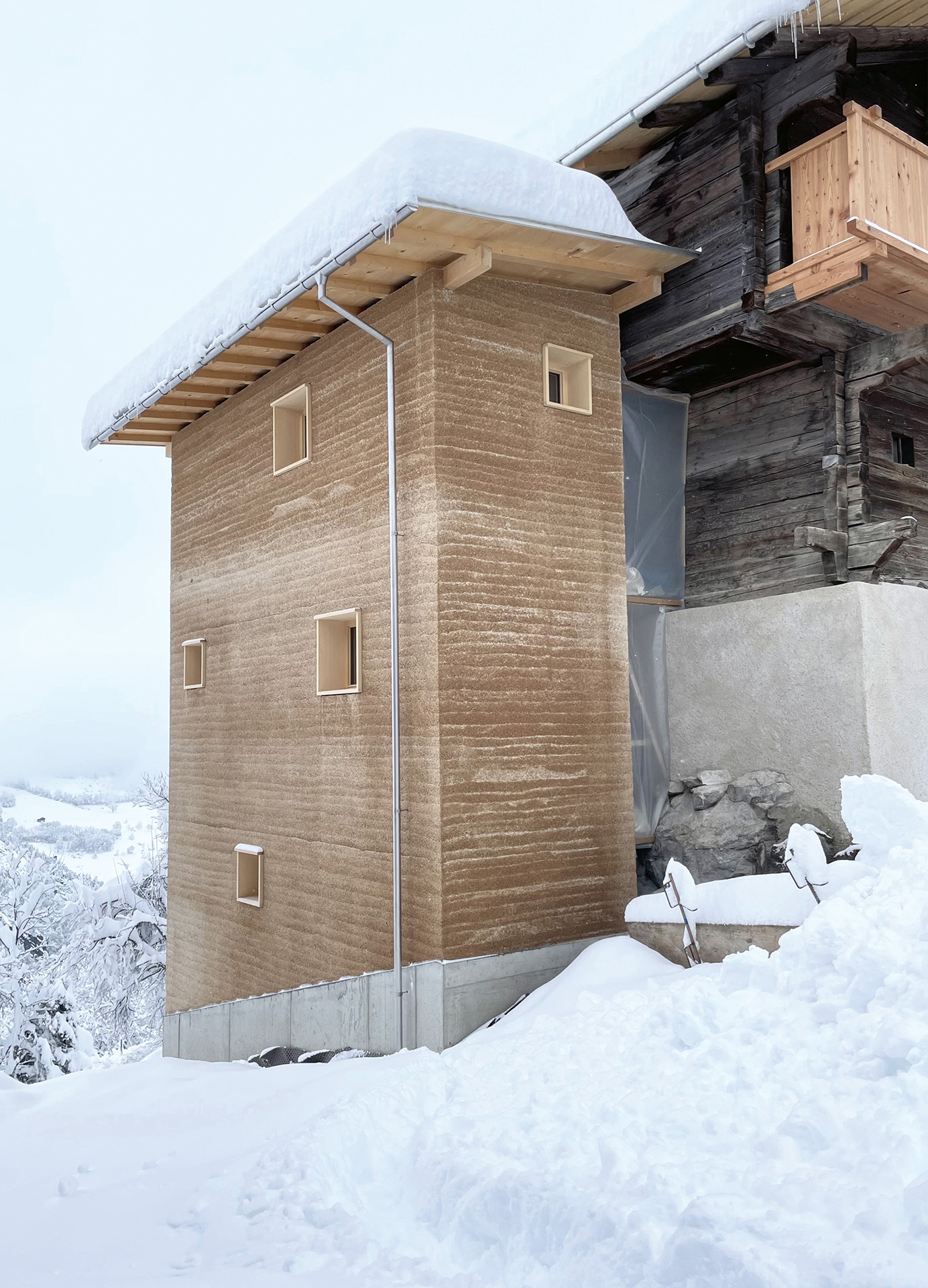 Das Waschhaus auf der Nordseite des Hauses beherbergt die Nasszellen. Die gestampften Hanfkalkwände nehmen die Horizontalität des Strickbaus auf.