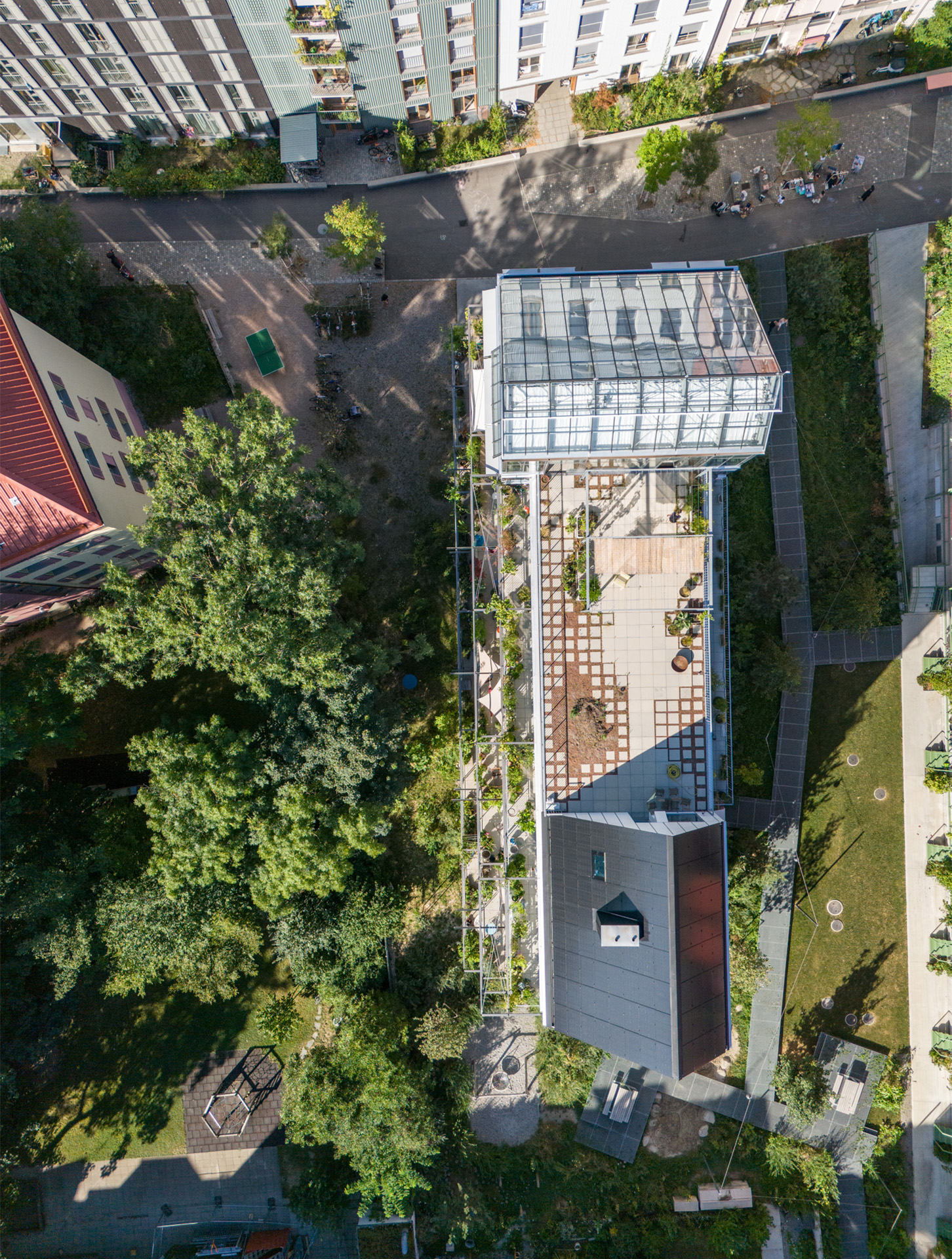 Blick von oben auf die Dachterrasse mit den zwei Aufbauten: Das gemeinschaftlich genutzte Glashaus und das Gasthaus.