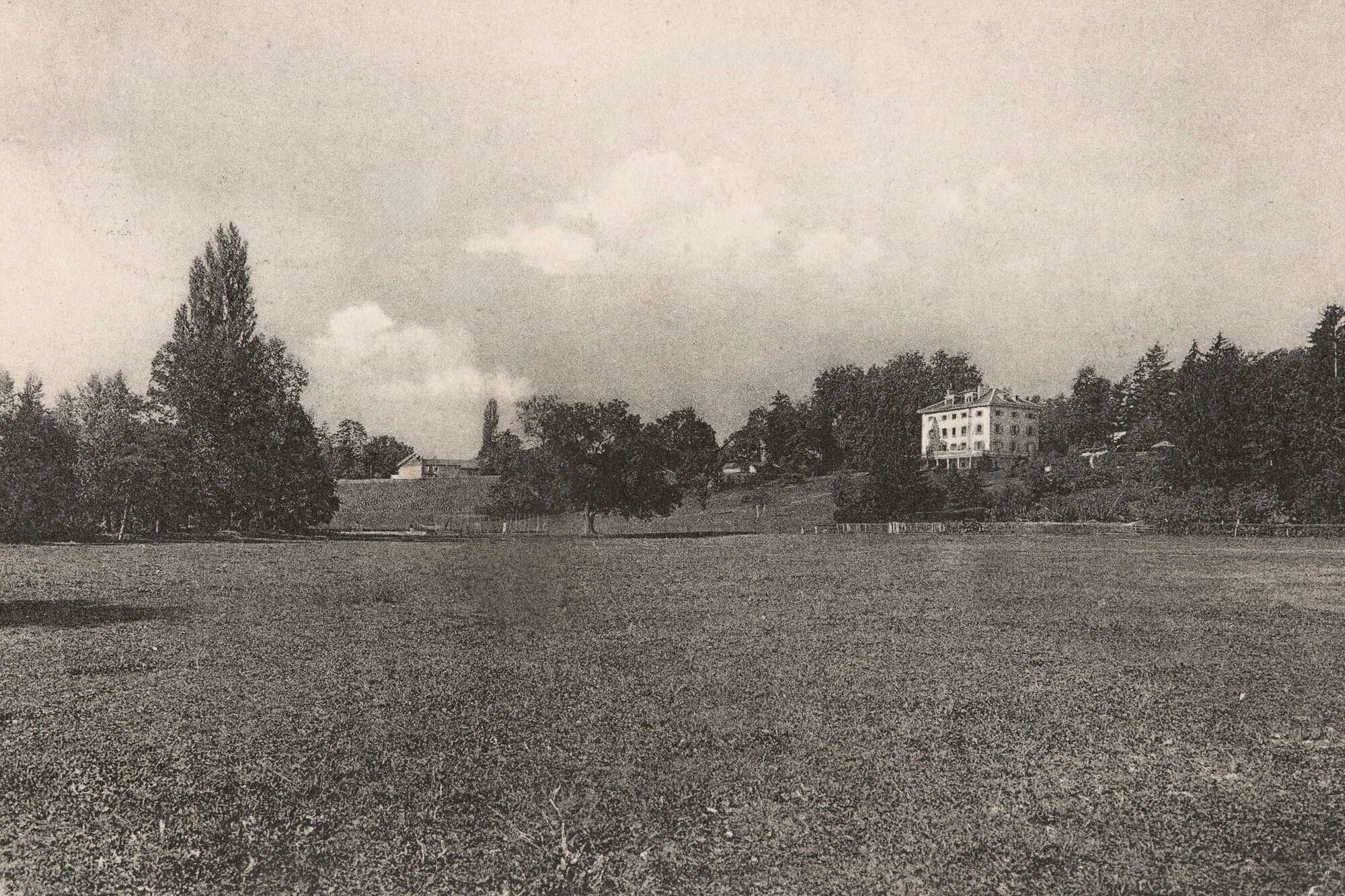 Sur cette photographie, prise au tournant du 20e siècle, l'on aperçoit la maison de maître des Pictet de Rochemont en arrière-plan, qui sera occupée successivement par le pensionnat Haccius (dès 1853), puis par la mairie de Lancy dès l'après-guerre. À l'époque de la prise de vue, la plaine de la Praille est encore recouverte de prairies et de terrains agricoles.