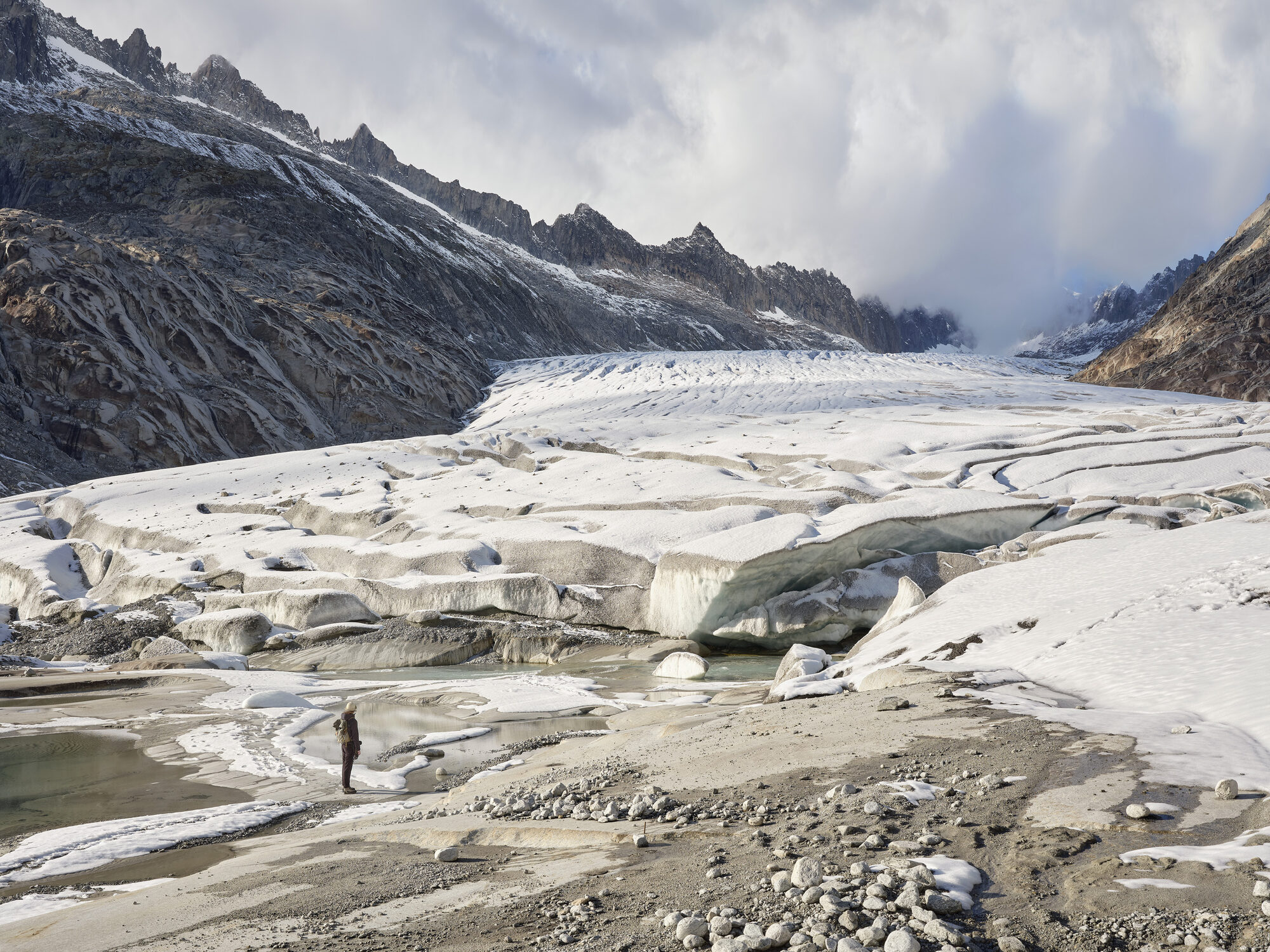 Randonneur·se face au glacier du Rhône, crevasses et moraine.