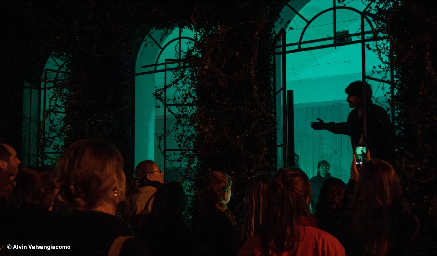 Installation nocturne sous une arcade végétalisée éclairée en vert, public rassemblé autour