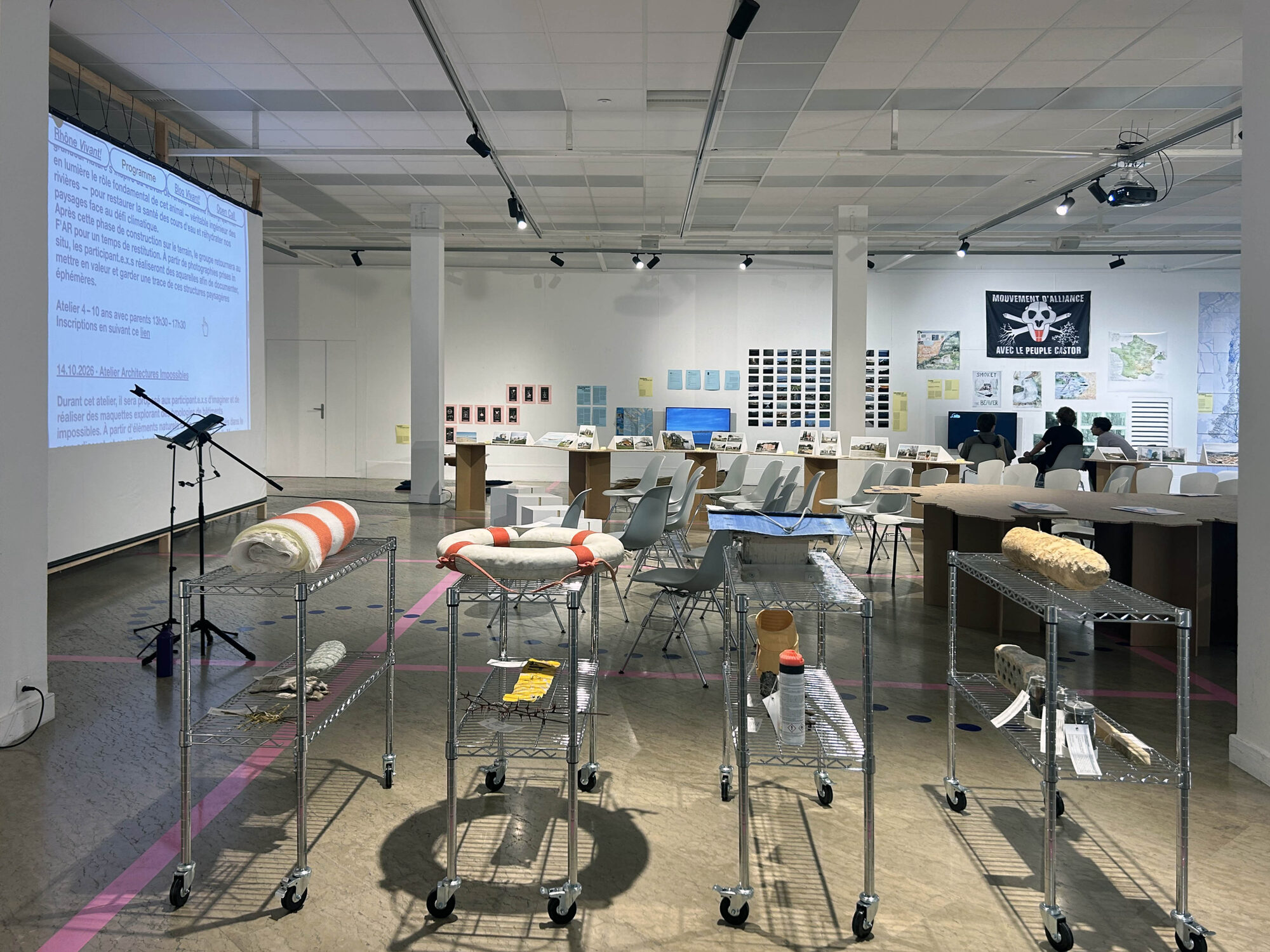 Chariots métalliques portant bouées, bois et objets étiquetés comme des pièces archéologiques, projection au fond de la salle.
