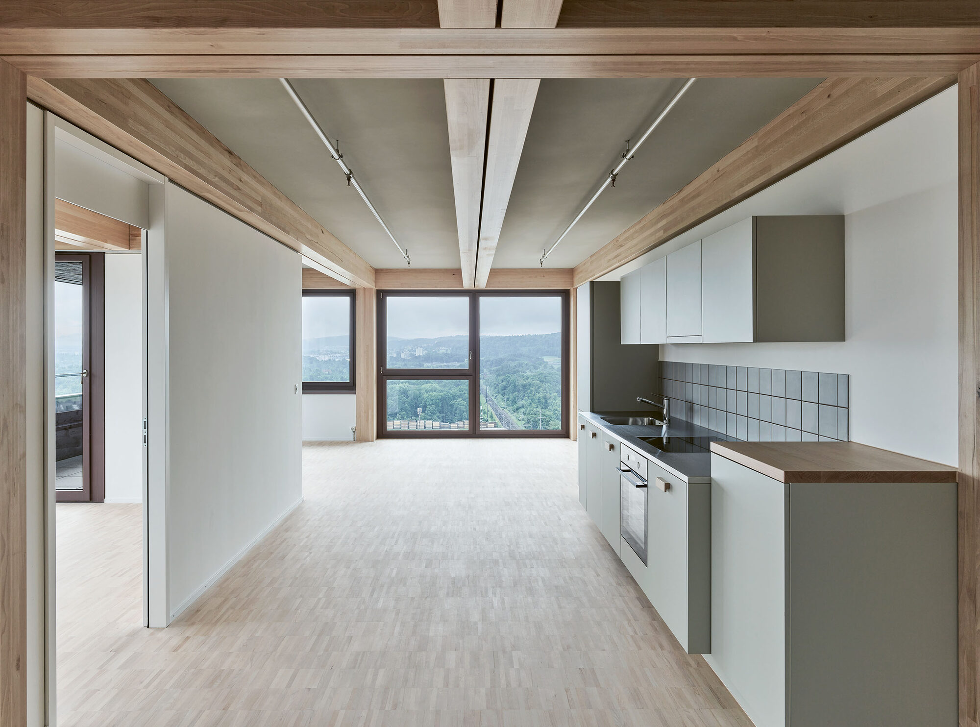 Cuisine ouverte d’un appartement de la tour H1 avec poutres en bois apparentes et vue sur la campagne.