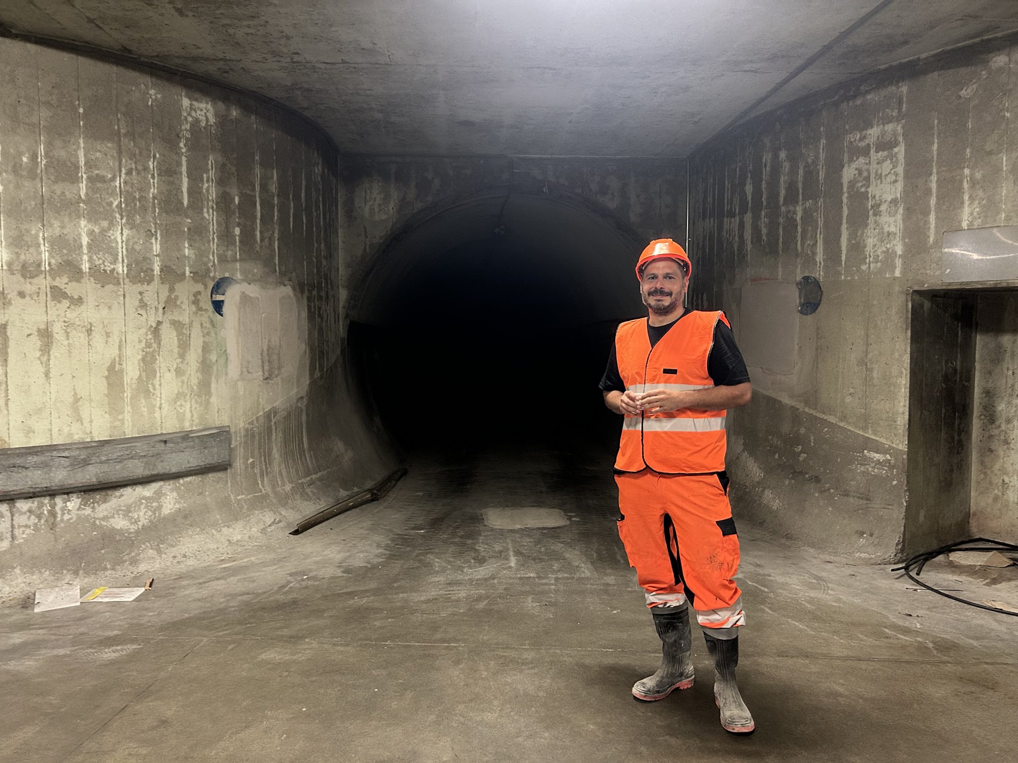 Homme en tenue orange de chantier debout dans un large tunnel en béton.