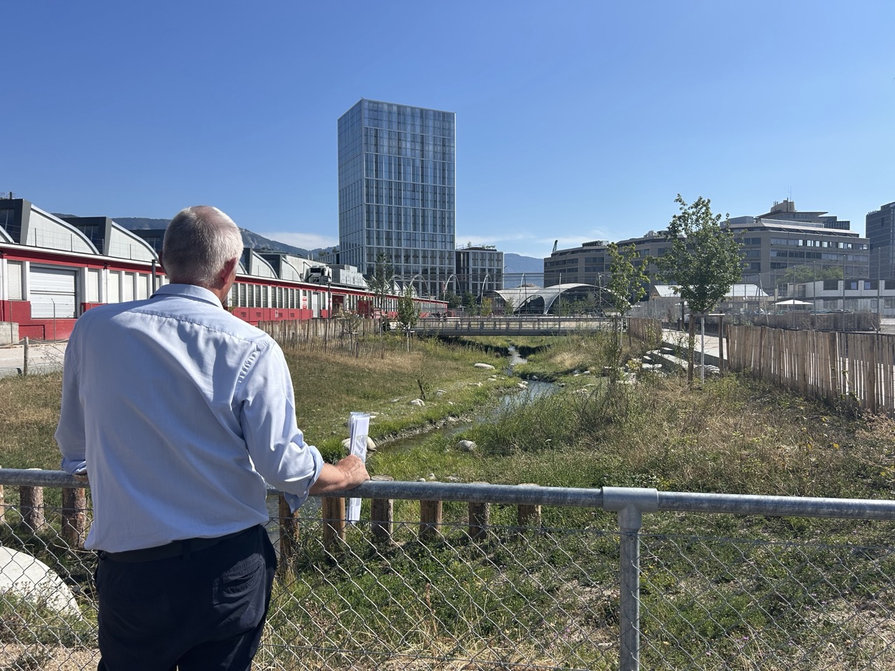 Marco Rampini regarde la Drize ouverte, avec une tour et des halles du PAV au fond.
