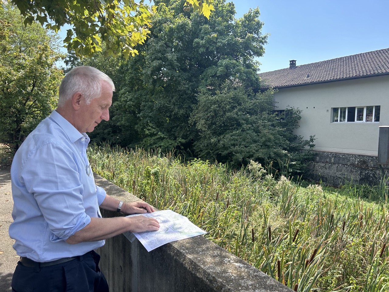 Marco Rampini consulte un plan, accoudé à un muret au bord de la Drize.