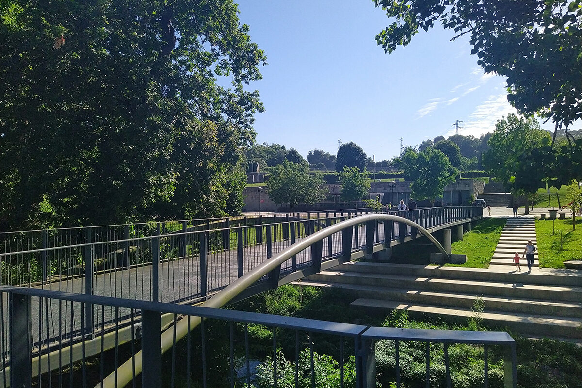 Passerelle en arc au-dessus d’un sentier, escaliers et végétation le long de la rivière Leça.