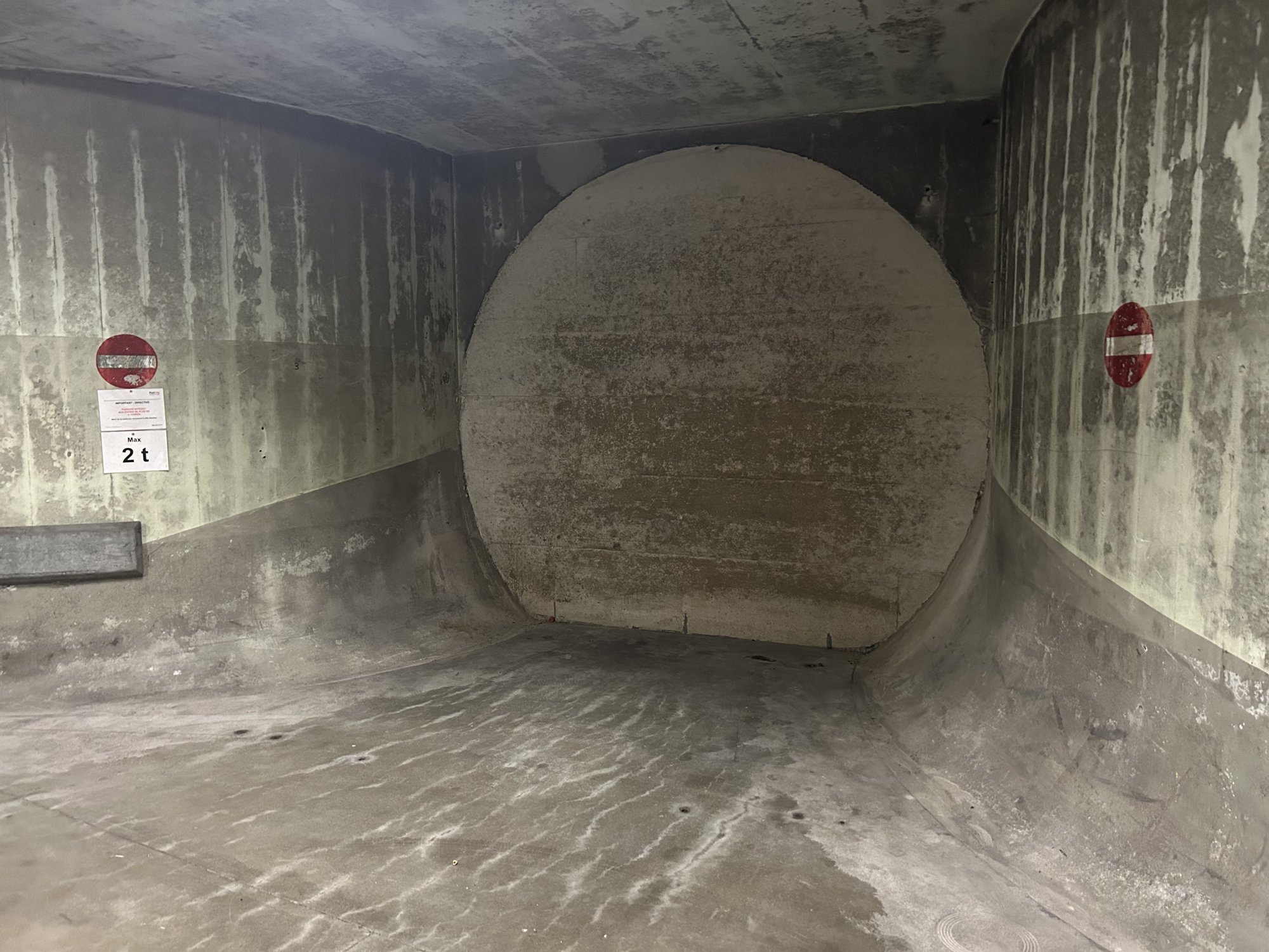 Galerie en béton fermée par une grande paroi circulaire.
