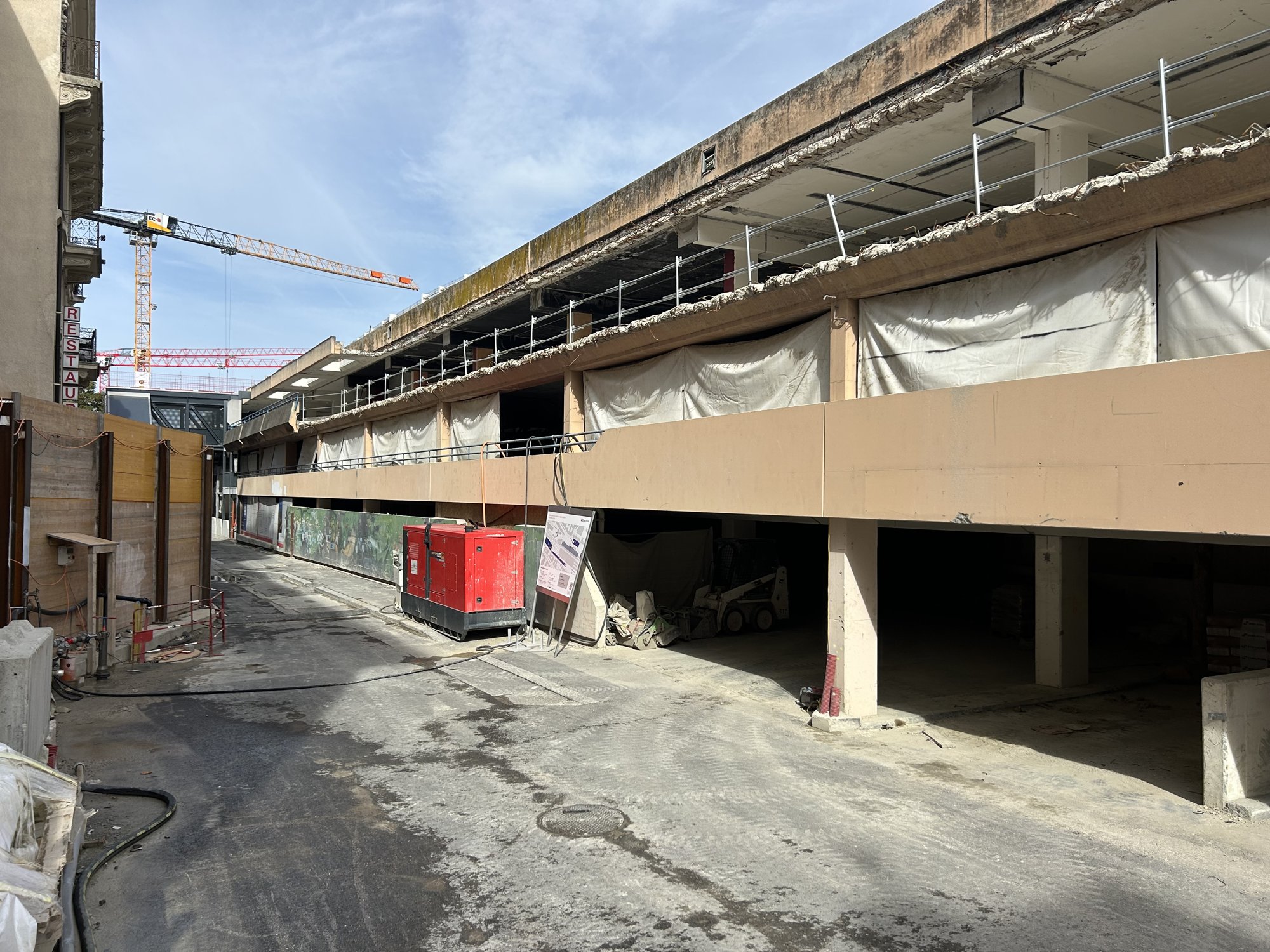 Étages d’un parking bâchés et partiellement démolis, grue en arrière-plan.