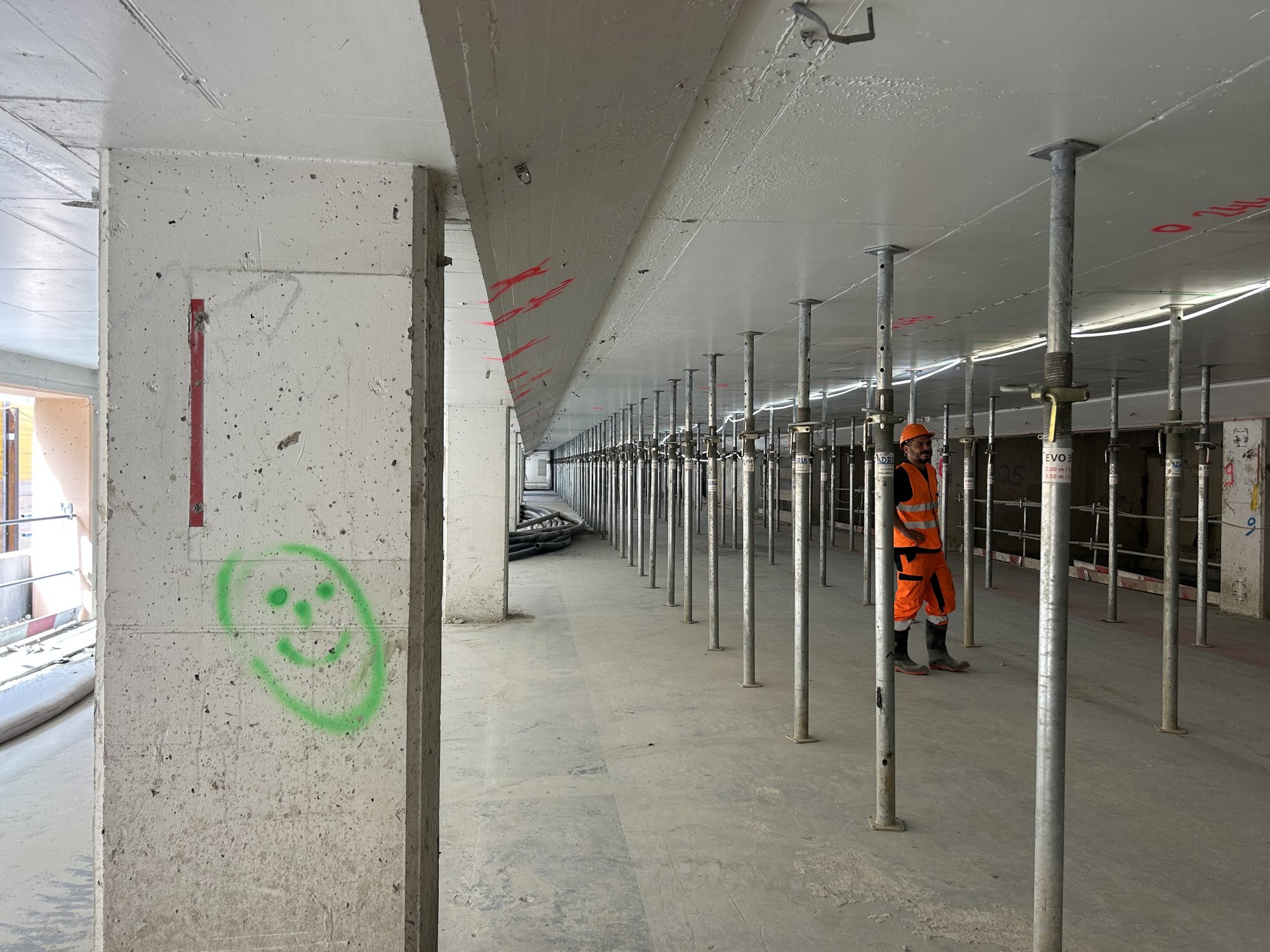 Pilier en béton portant un smiley vert, rangées d’étais métalliques au fond.