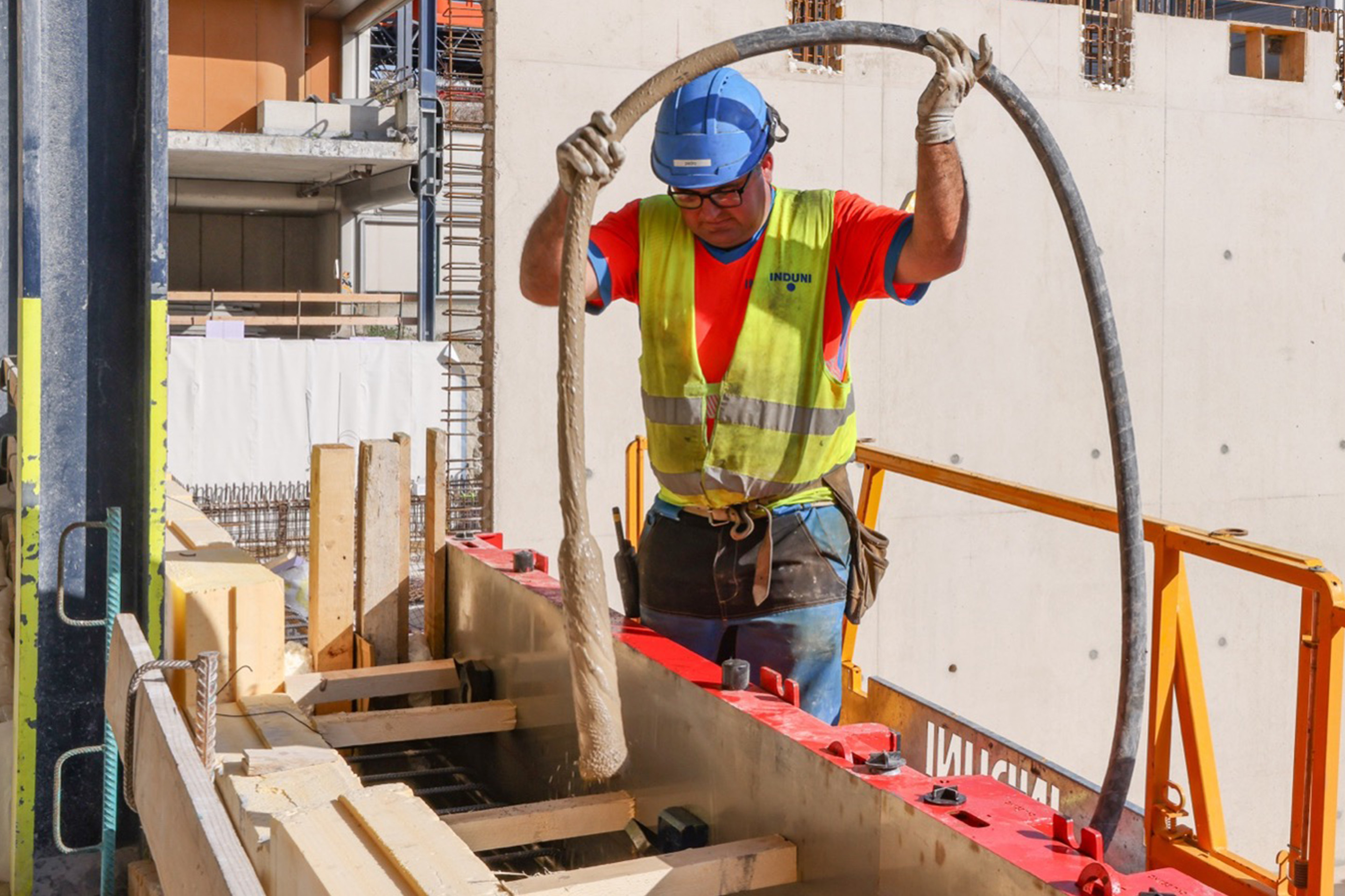 Rütteln von LC3-Beton auf der Baustelle des Doppeldeckerprojekts im Jahr 2026. Im Hintergrund eine fertige Wand aus LC3-Beton. 