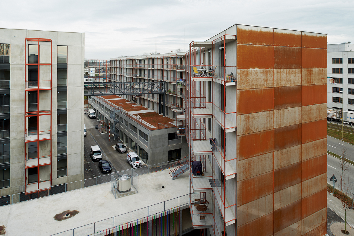 Die roten Stahlstrukturen der Balkone und Laubengänge werden in Zukunft mit Pflanzen bewachsen sein und so das Quartier begrünen.