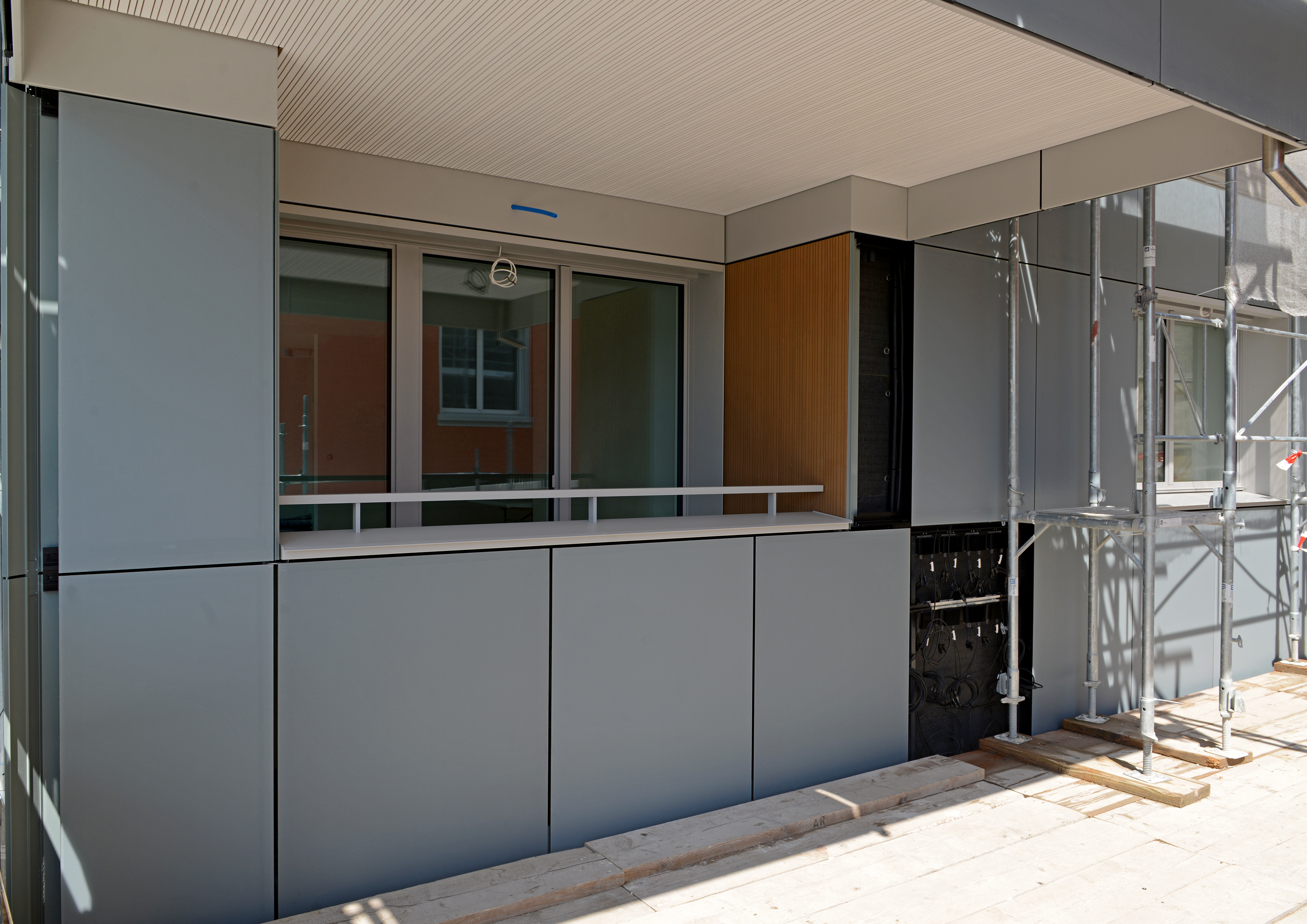 Ansicht der bereits montierten grau-grünen Glasfassade, mit den integrierten PV-Modulen.