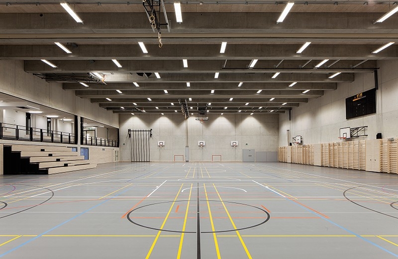 Dreifachturnhalle mit Zuschauertribüne: Eine hocheffiziente LED-Beleuchtung verbraucht rund ein Drittel weniger Strom als vergleichbare konventionelle Anlagen, und eine Solarstromanlage auf dem Dach soll rund die Hälfte des Energieverbrauchs der Schulanlage selbst produzieren.