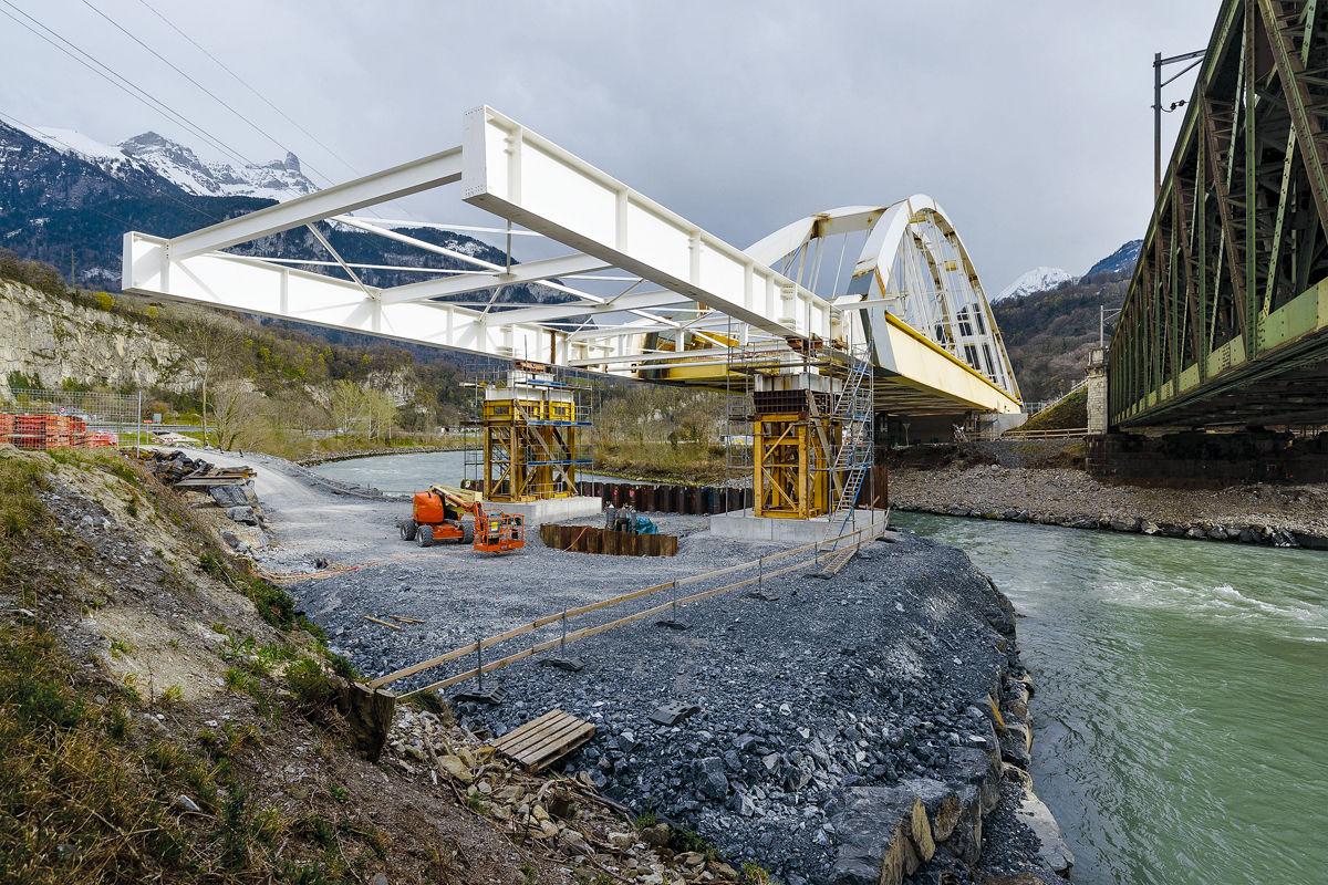 Der 30 m lange Vorbauschnabel hat die provisorischen Pfeiler am rechten Rhoneufer (Fliessrichtung von links) erreicht. Nach dem weiteren Vorschub über den Fluss wird die Brücke stromabwärts gegen die bestehende Fachwerkkonstruktion verschoben.