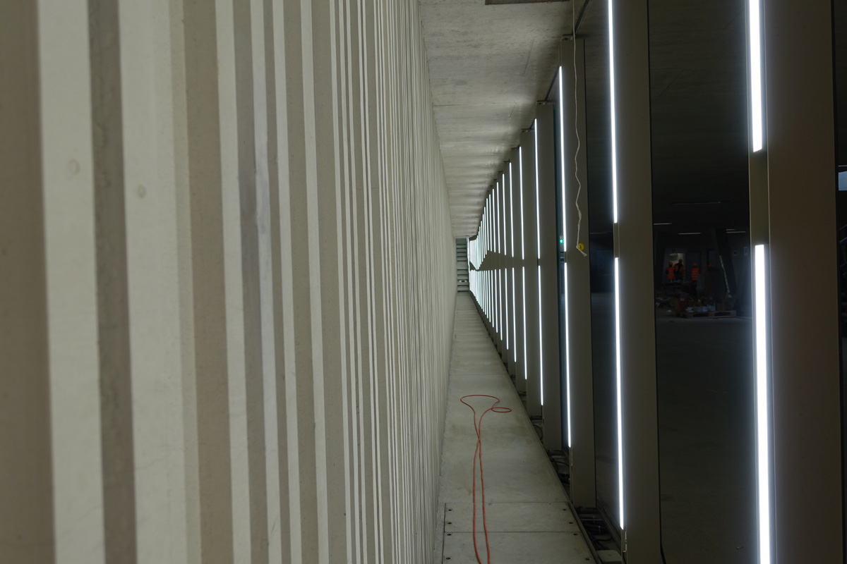 Das Innenleben der Lichtwand, die die Quartierverbindung für die Fussgänger beleuchtet. Die Hinterseite aus Beton und die Abdeckgläser wurden mit einem gleichartigen Streifenmuster vesehen, was beim vorbeilaufen einen tanzenden Effekt erzeugt.