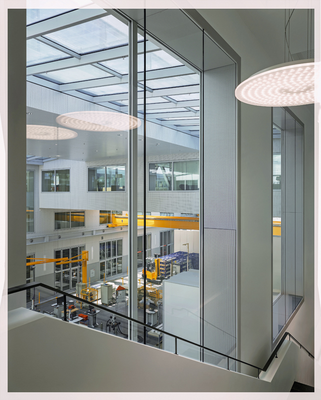 Das Tragwerk der Verbindungsgänge ist als Brücke ablesbar und das zentrale Element des Gebäudes: Es gliedert das Volumen, vermittelt zwischen Bürotrakt und Versuchshalle und stellt den räumlichen Bezug her.