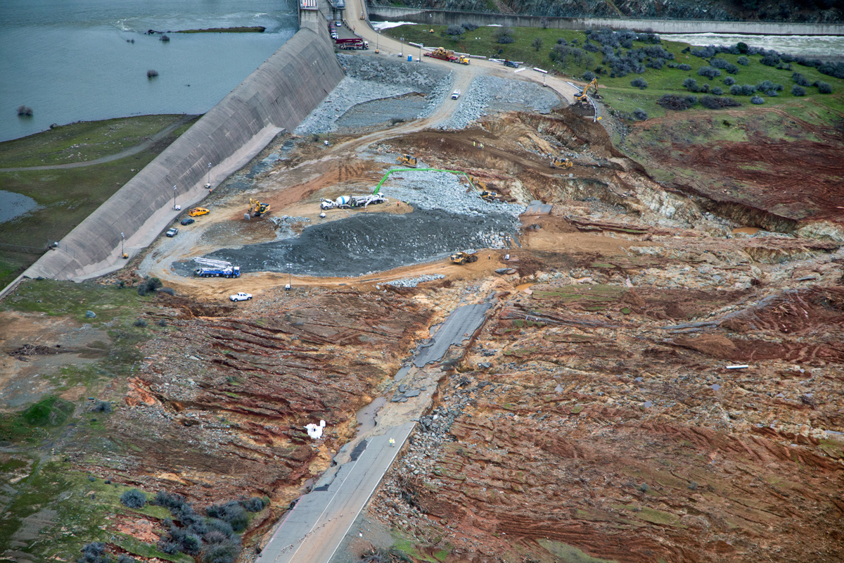 Luftansicht der erodierten Landschaft unterhalb des Dammüberlaufs, im Hintergrund die beschädigte Hochwasser-Notentlastung. Durch diesen Kanal fliessen weiterhin 100.000 Kubikfuss (2.831.700 l) pro Sekunde Wasser ab, um das Niveau des Sees zu senken.