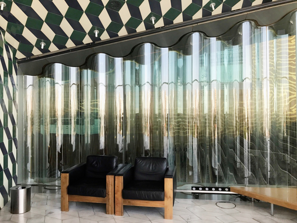 Die gewellte Doppelverglasung umgibt ein Vakuum. Im Bild die kleine Variante gegen ein Foyer hin. Die gleiche Massnahme wurde auch bei den grossen Verglasungen im Saal gegen die Strasse hin angewendet.