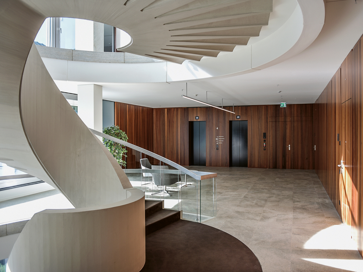 Eine skulpturale Wendeltreppe verbindet die zentrale Schalterhalle mit dem Besprechungsbereich. Böden aus Muschelkalk und Wände in Schweizer Birnbaum verleihen dem Innern ein zurückhaltendes und zugleich nobles Erscheinungsbild.