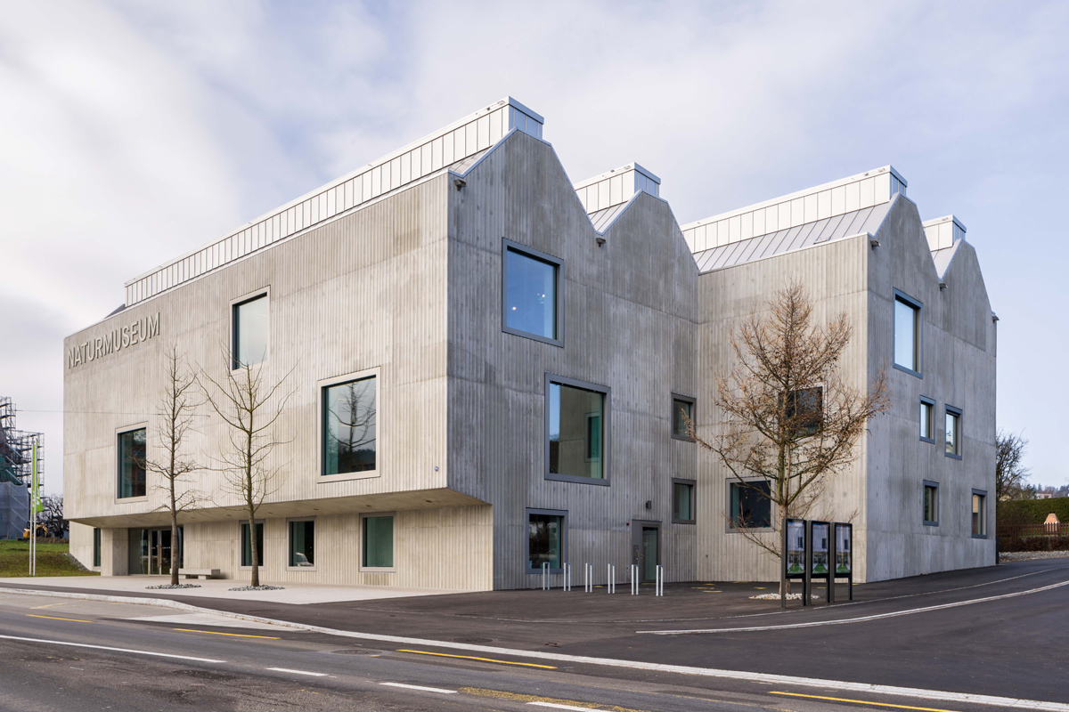 Im wechselnden Licht zeigt sich der Charakter der gerillten Betonfassade. Die Rücksprünge im Volumen bilden Plätze um das Haus.