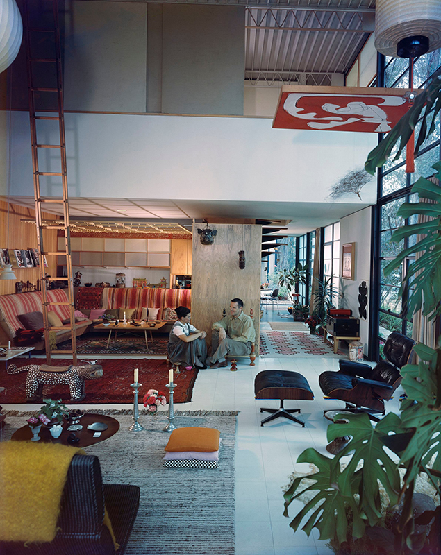 Charles und Ray Eames im Wohnraum ihres Hauses. Die streng modular aufgebaute Konstruktion aus Stahl, Glas und Holzplatten ist gefüllt mit Möbeln, Objekten und Sammlungsstücken der beiden Designer. Aufnahme von 1958.