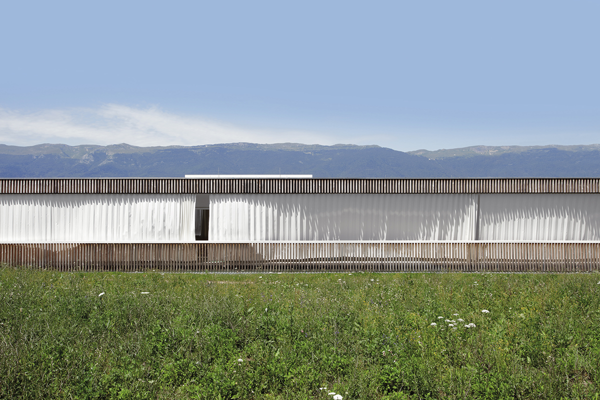 Im Vordergrund zeichnet der eingeschossige Bau einen Strich in die Landschaft, im Hintergrund zeichnet sich der Jura ab.