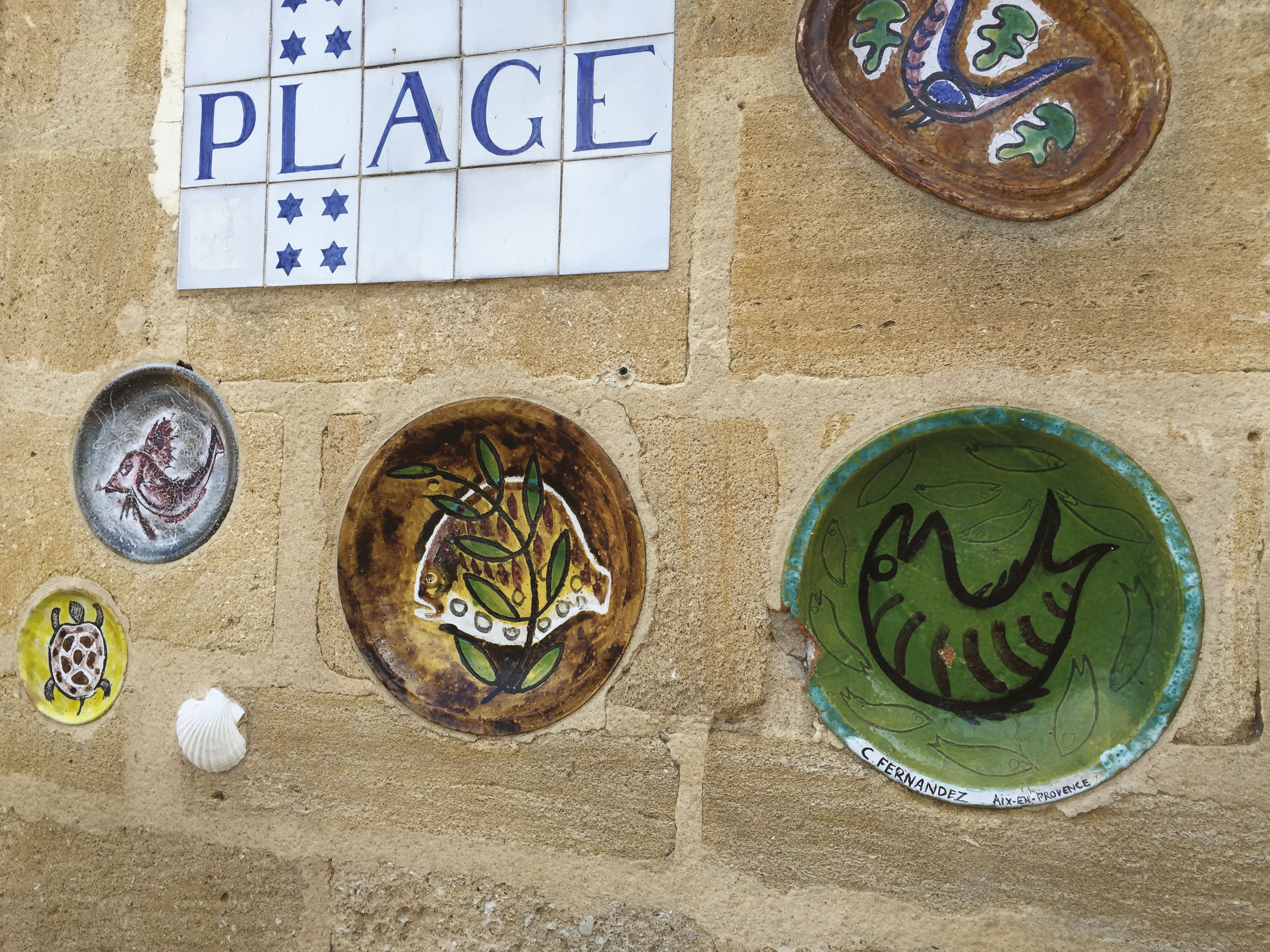 Les œuvres des artistes proches de Fernand Pouillon sont présentes dans tout le hameau : des sculptures, des céramiques incrustées dans les façades. Ici, l’enseigne de l’hôtel Provence Plage de Philippe Sourdive et les plats en céramique de Carlos Fernandez.