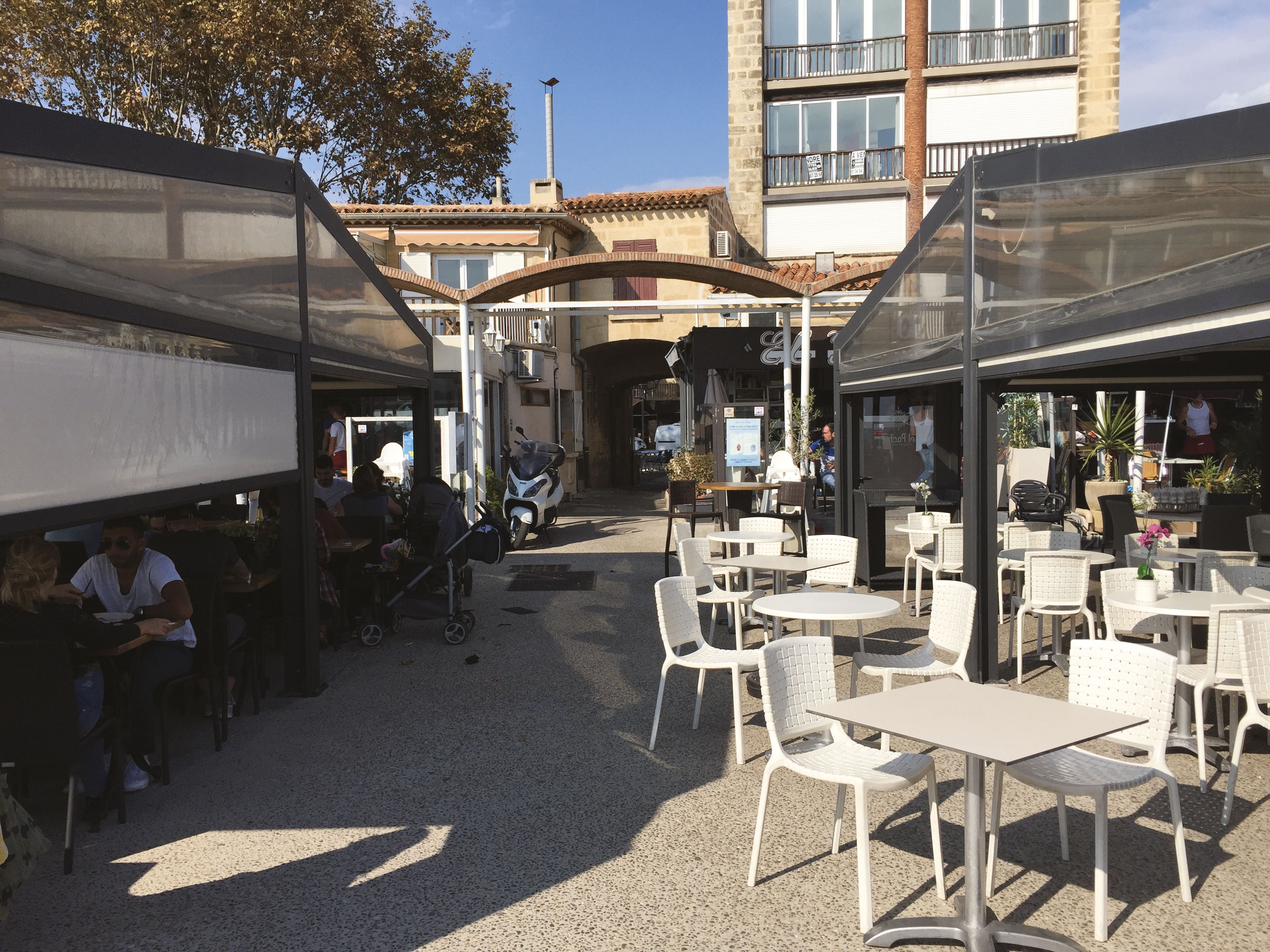 Pour tenter de régler la question de l’implantation anarchique de terrasses couvertes, la commune a établi avec le Conseil d’architecture, d’urbanisme et de l’environnement (CAUE) du Var un schéma d’aménagement des terrasses extérieures de l’Esplanade Bœuf. On voit ici des structures démontables en métal et PVC, dont l’installation est coordonnée par un architecte et soumise à autorisation et à redevance, et au second plan les passages couverts en briques et piliers métalliques des